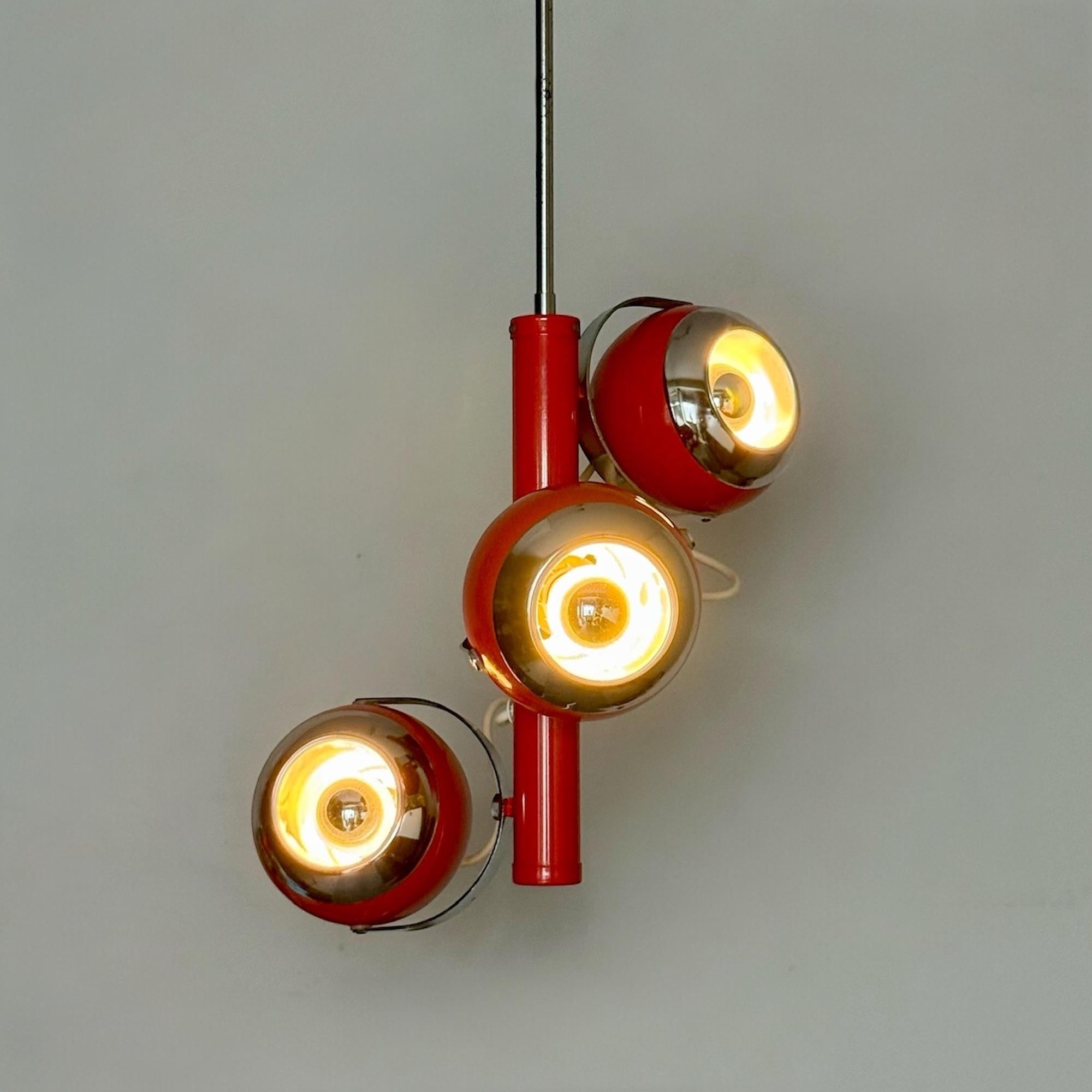 Lampada a sospensione degli anni '70 con tre faretti a forma di occhio in metallo smaltato rosso con finiture cromate, montati su una struttura centrale rossa coordinata. L'opera è sospesa a un'asta cromata e include il baldacchino originale del