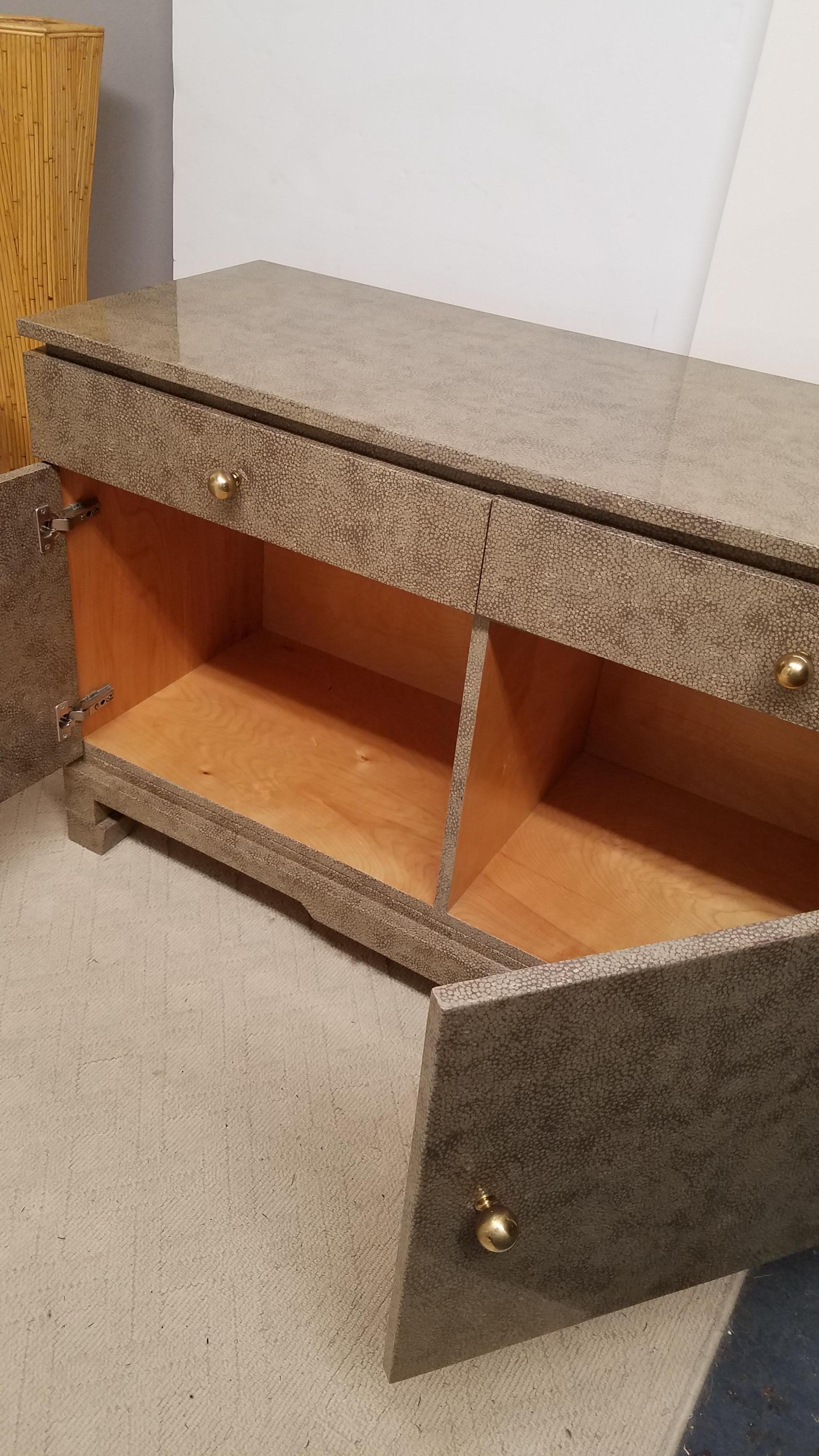 An Asian faux shagreen wrapped server credenza with 2 drawers and 2 doored cabinet below. Polished brass ball hardware with a high gloss finish. Custom decorator piece attributed to Karl Springer.