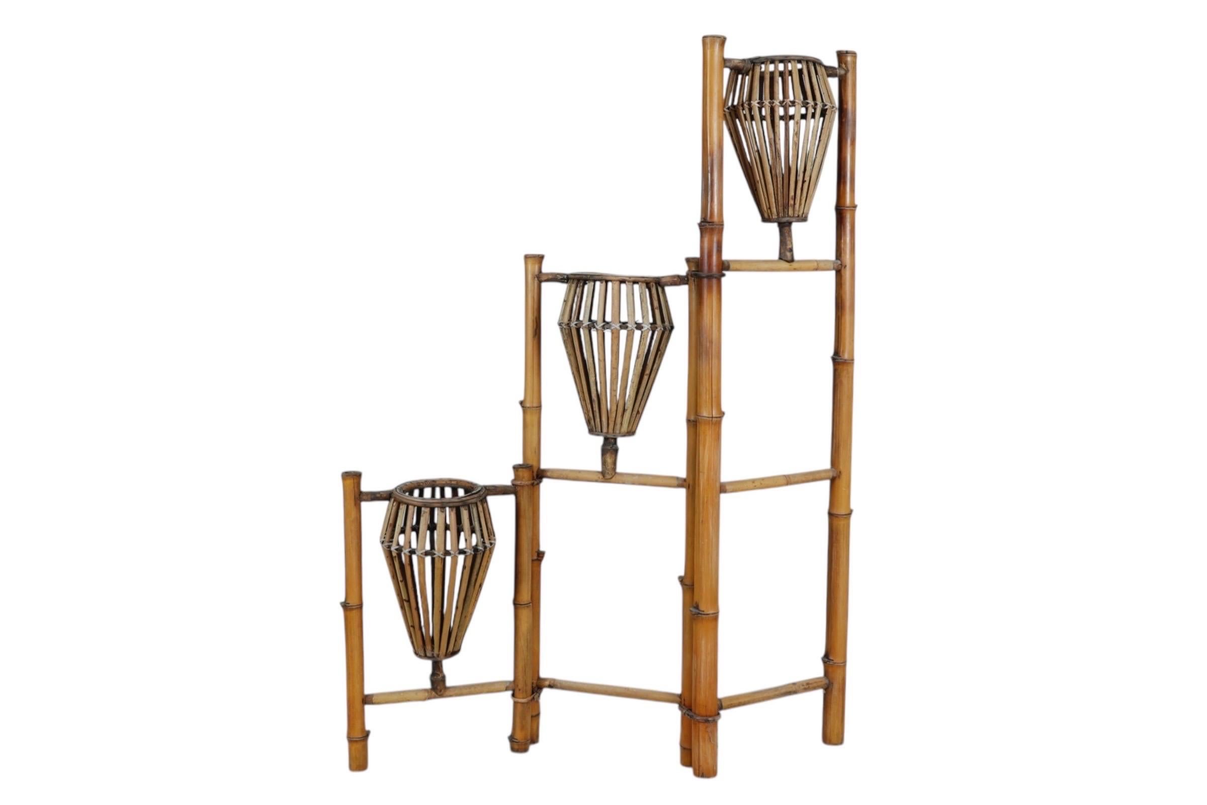 Un porte-plante pliant en bambou des années 1970. Trois vases en forme de lanterne sont fixés à l'aide d'épingles et de rotin à des cadres en échelle de bambou à des hauteurs graduées. Les échelles se plient en accordéon pour que les vases