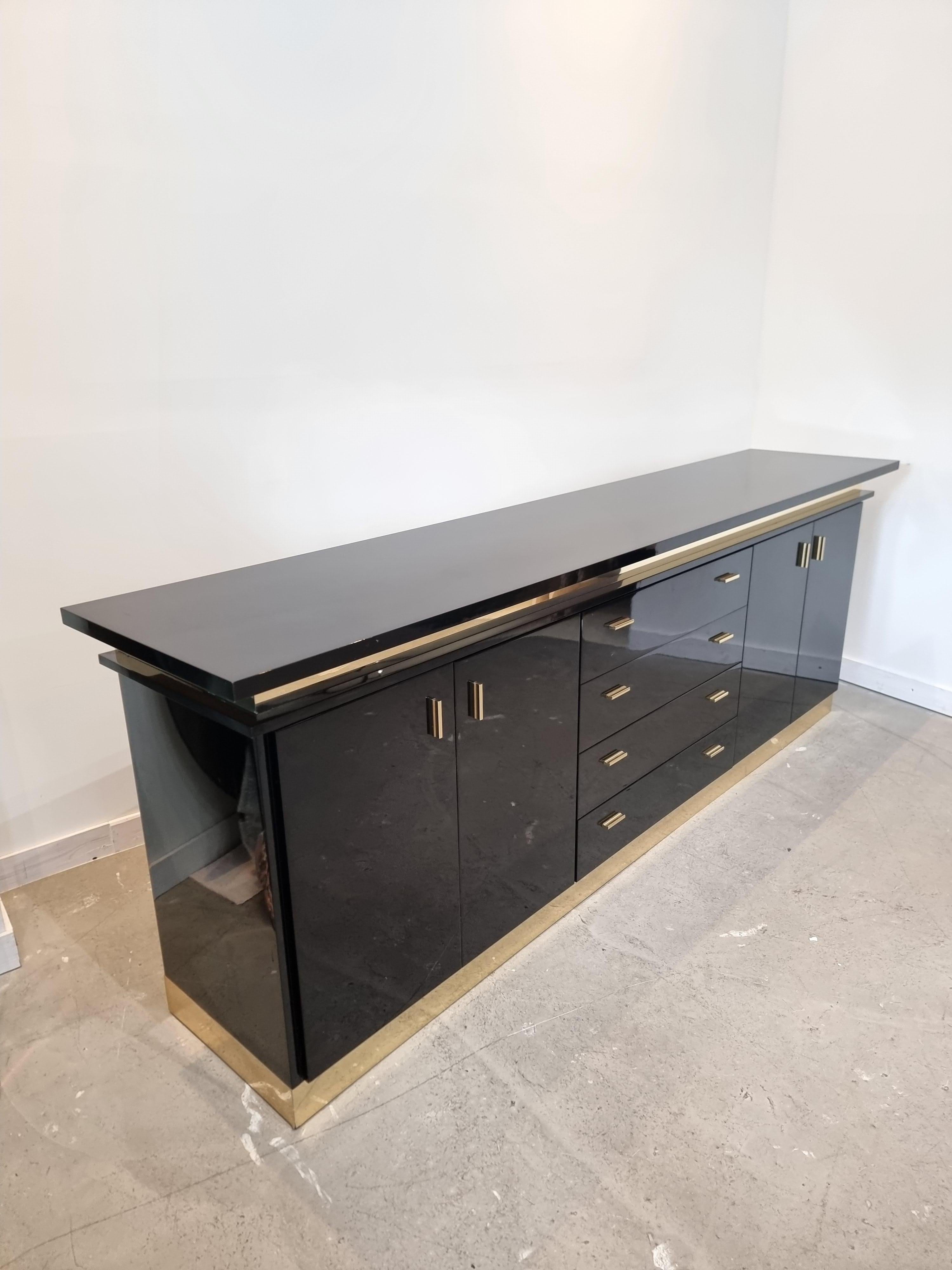 Stunning black lacquered sideboard by Jean Clause Mahey, France, 1970s. High quality piece, wooden base finished in a high gloss black lacquer and chic golden/brass details.

Provided with four doors and four shelving units, middle section.

In