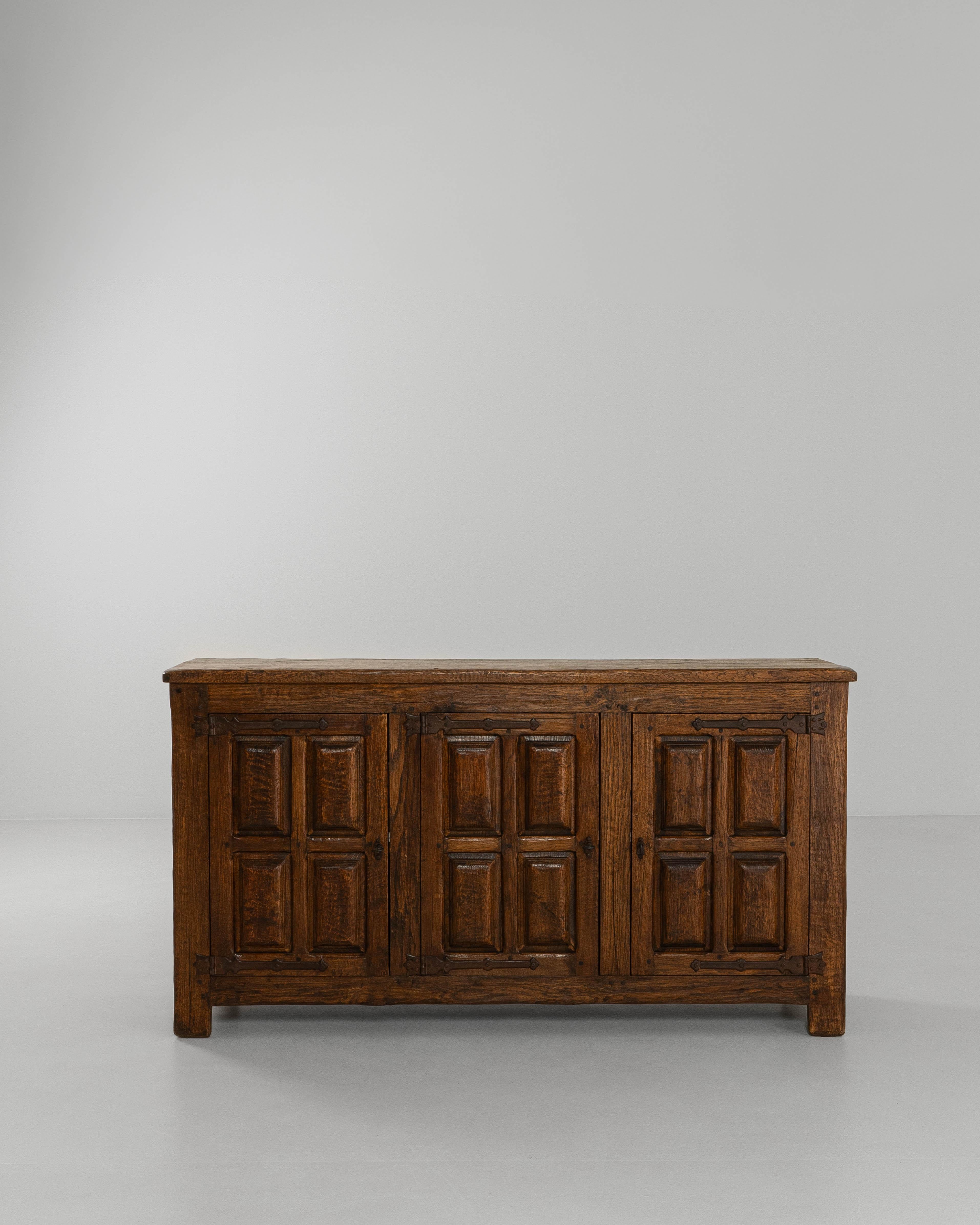 This 1970s French Baroque oak buffet presents a bold yet grounded presence, blending traditional decorative influences with robust, functional craftsmanship. Constructed from solid oak, the piece showcases deeply molded paneled doors that reference