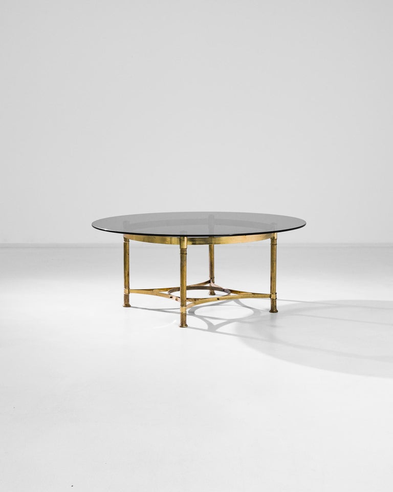This circular coffee table brings an air of sophistication to a space. Made in France in the 1970s, a frame of polished brass supports an amber tinted glass tabletop. This contrast of materials — the bright gold of the metal, the subtle opacity of