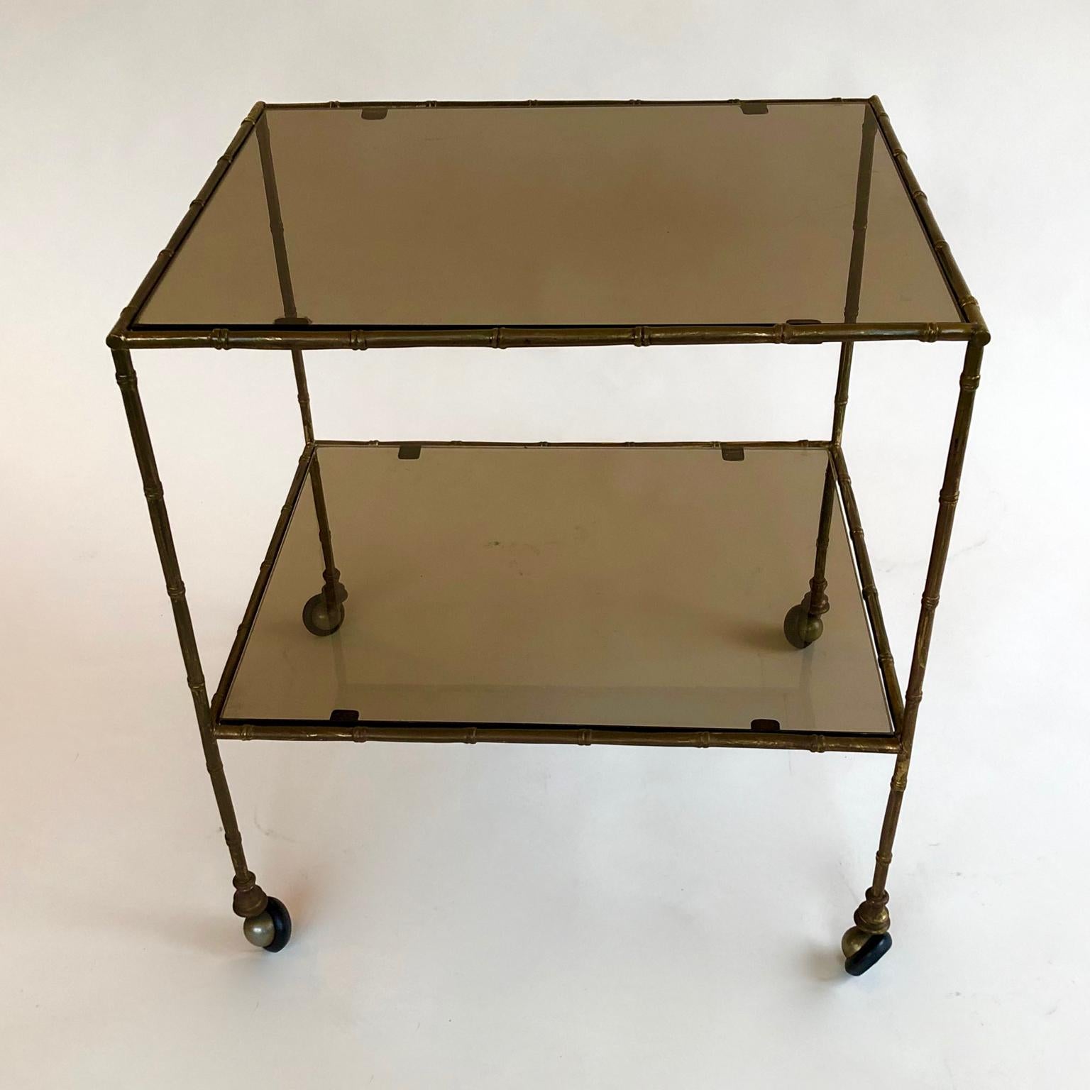 A stylish 1970s French brass faux bamboo and smoked glass 2-tier accent, side or end table, drinks trolley or cart. Possibly by Baguès. Untouched, unpolished. on wheels.