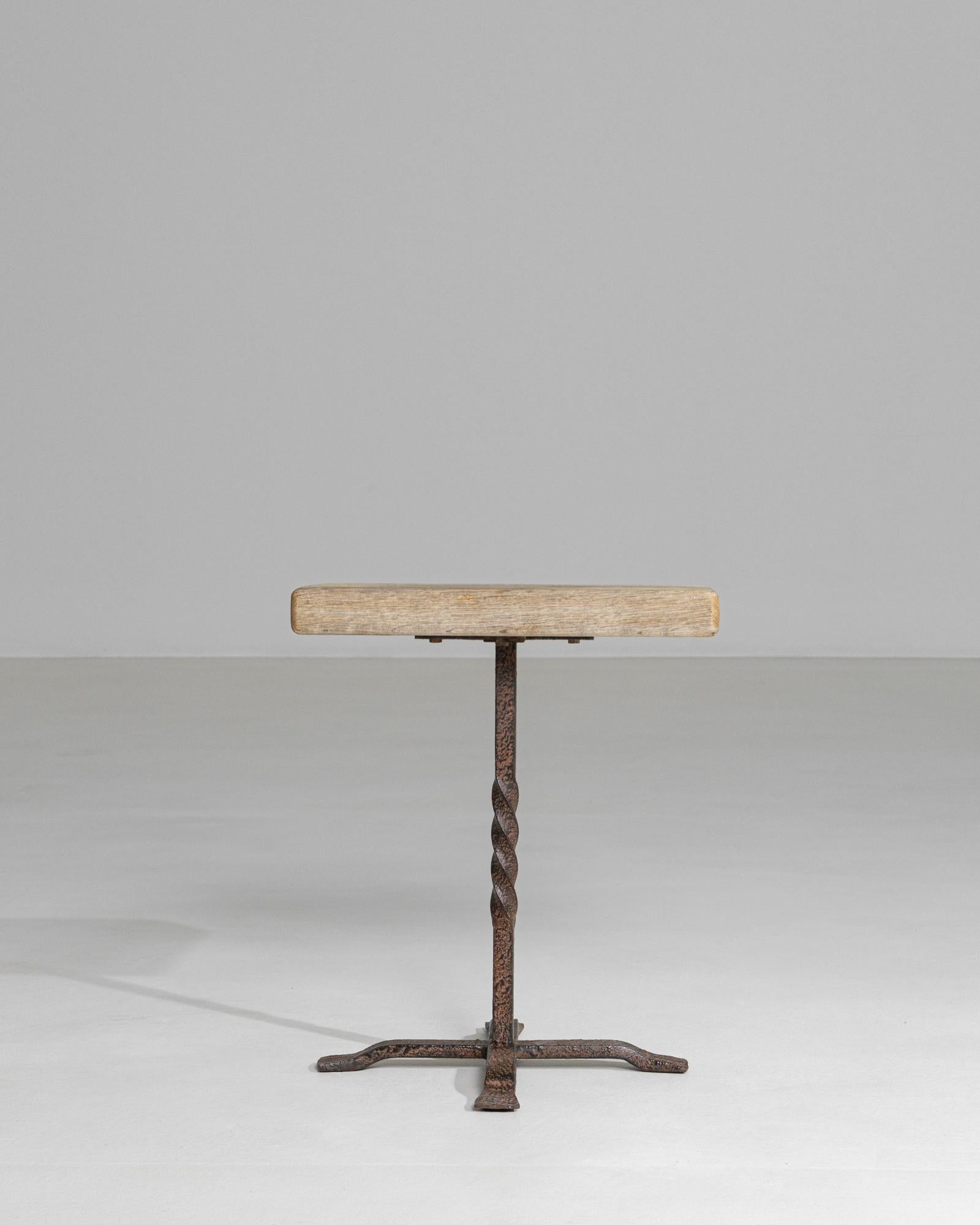 This striking French side table from the 1970s embodies the raw, sculptural character of the Brutalist movement. Featuring a solid, lightly patinated wood top, the table is supported by a twisted iron pedestal base that introduces strong vertical