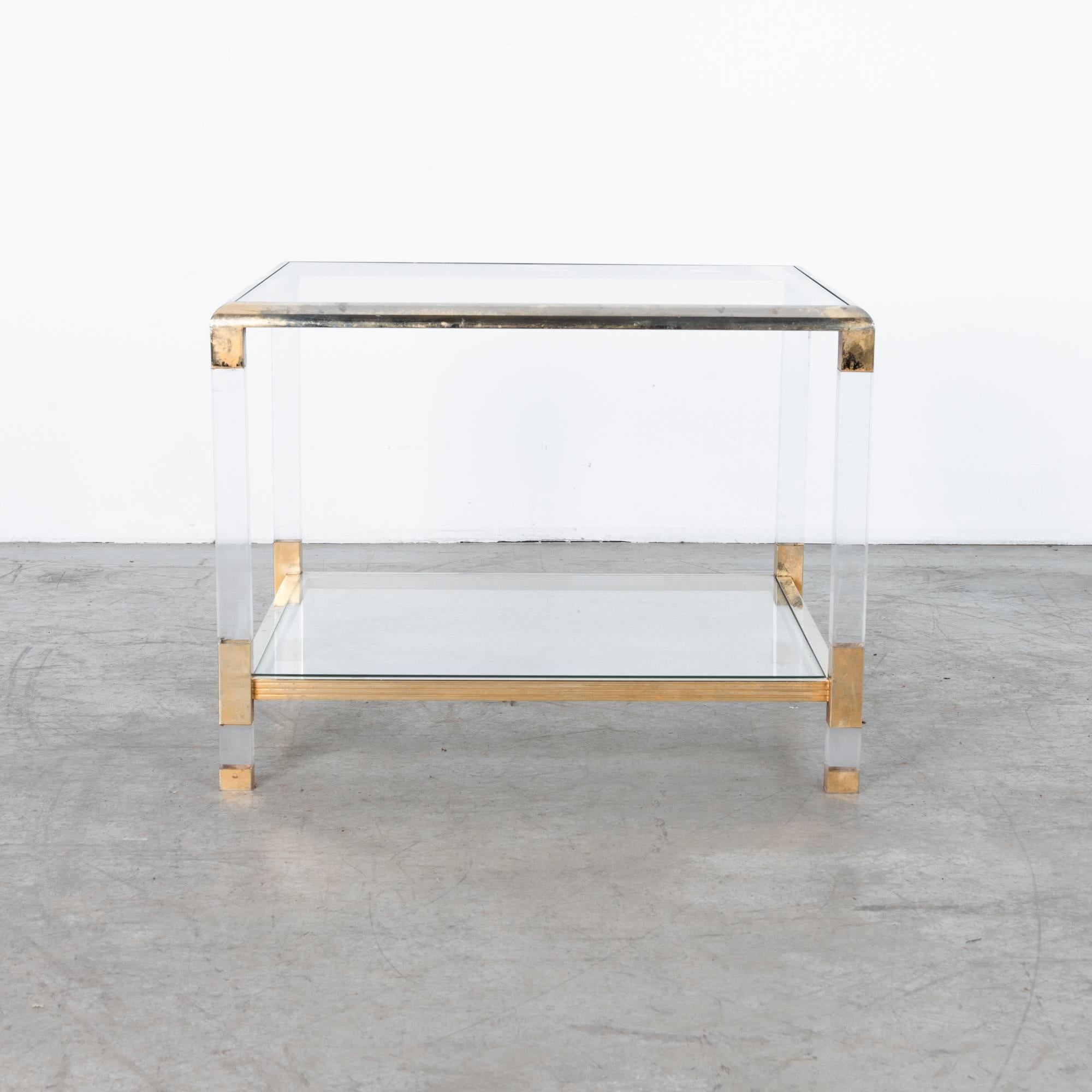 A classic and chic design from 1970s France. Combines resin casted transparent legs with brass-plated metal and glass table top and shelf for a sleek and clean finish. With a worn patina, this piece is clean while also recalling an elegance gone