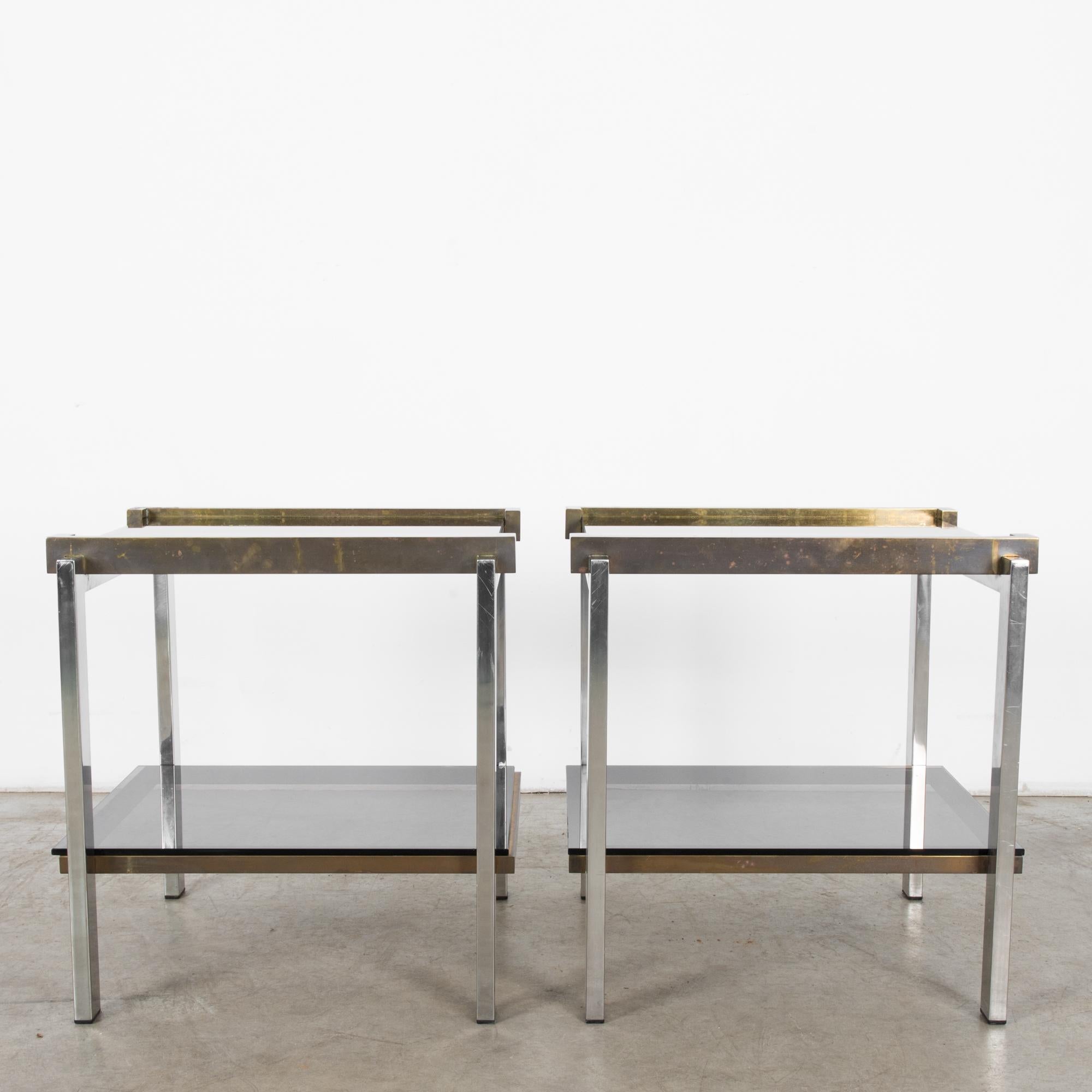A pair of glass topped metal side tables from France, circa 1970. Their tinted glass tops seem to float atop gleaming chrome legs in oxidized brackets. Chic and commanding presence in clean geometric outline, this decidedly modern pair carries