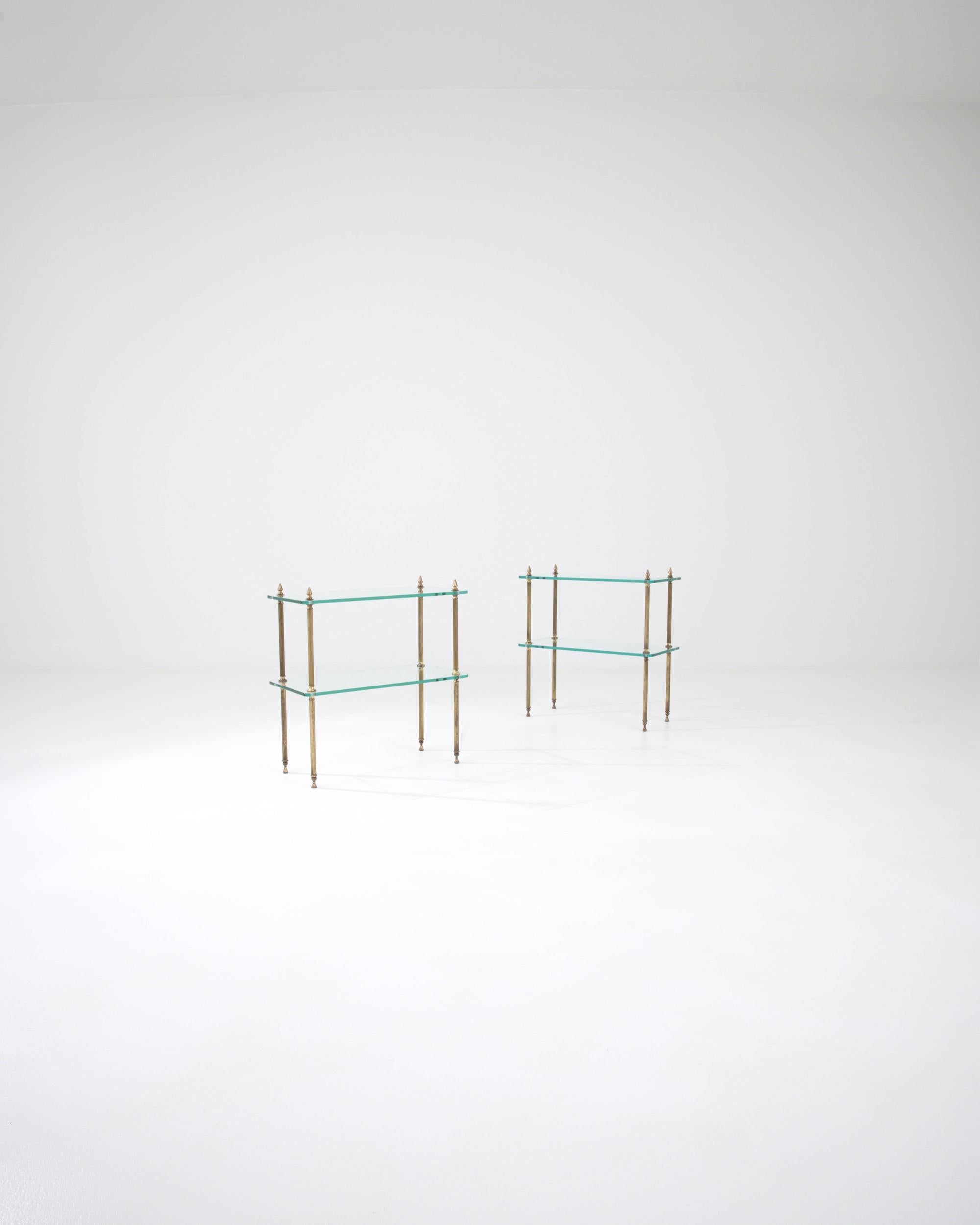 This pair of 1970s French side tables exudes the eclectic spirit of mid-20th Century experimentation. A double-decker glass structure, connected by fluted brass legs, showcases a practical yet original design, providing extra space for display. The
