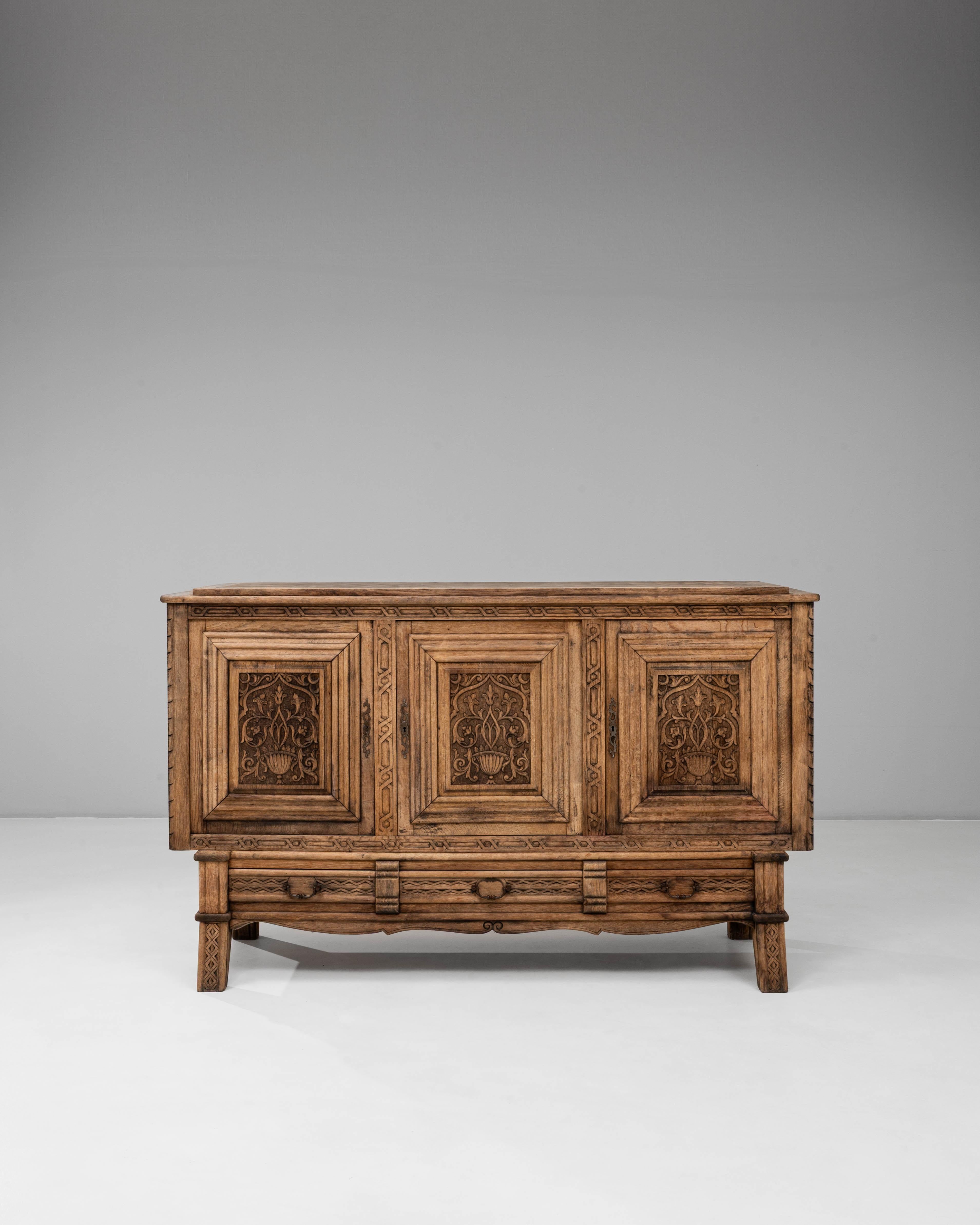 This 1970s French Gothic Revival carved oak sideboard showcases detailed craftsmanship inspired by medieval architectural motifs. The front panels feature intricately carved floral and foliate designs framed within raised geometric borders, creating