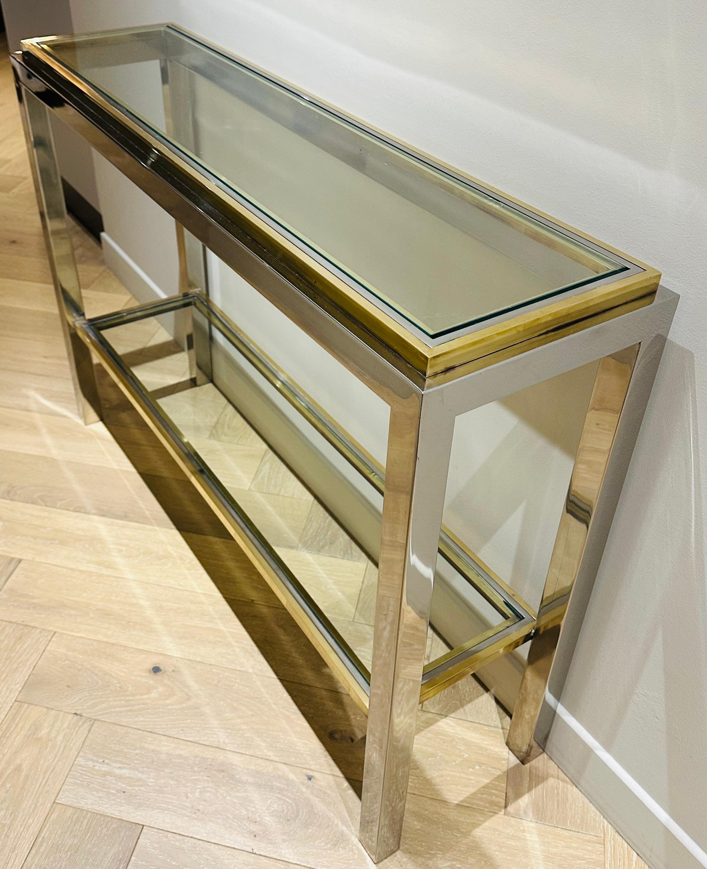 1970s French Maison Jean Charles brass, chrome and glass slim console table.  Two-tiered with clear glass bevelled shelves which float within the polished chrome and brass frame.  Signed 