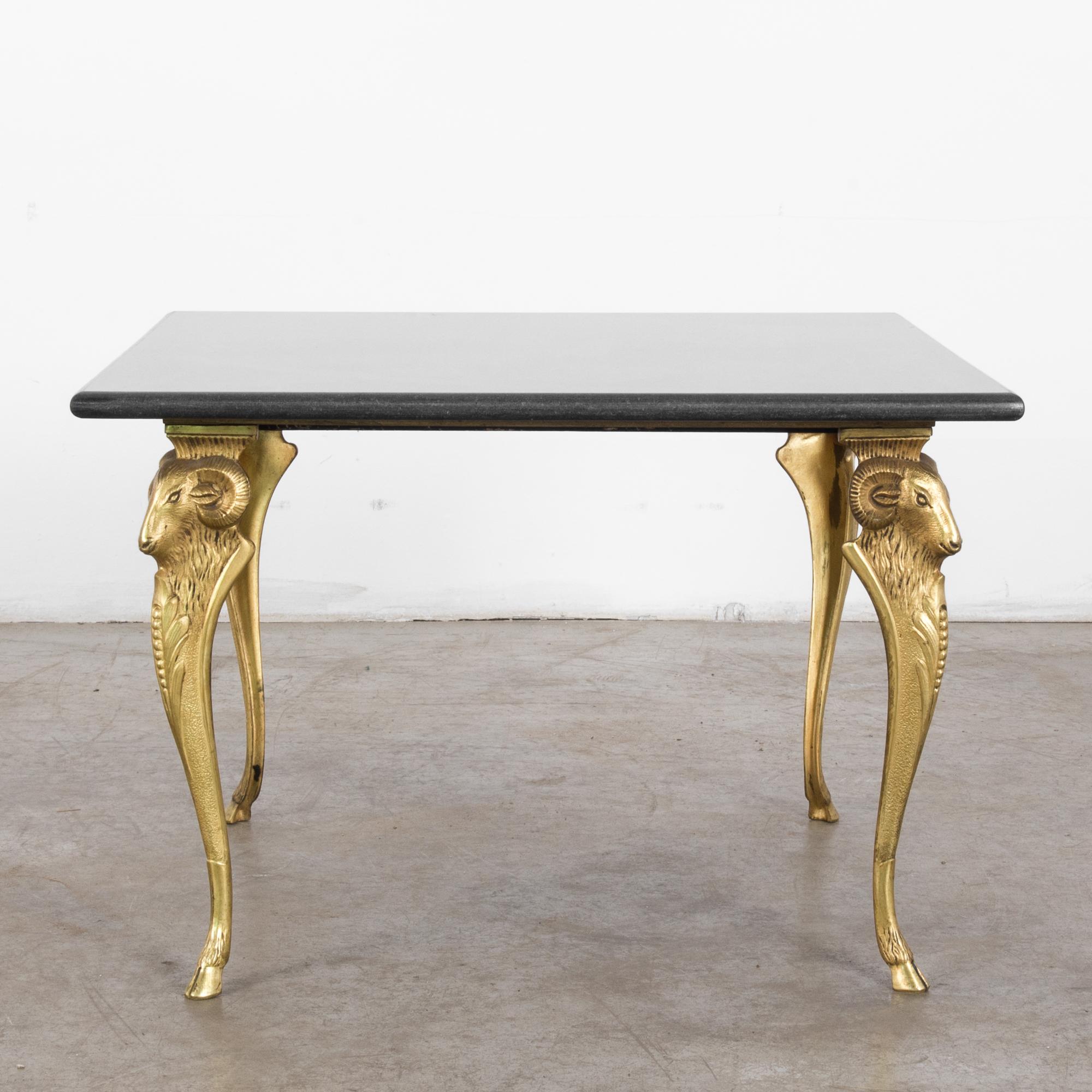 A marble topped metal coffee table from France, circa 1970. The deep gray marble top is supported by sculpted golden legs in the shape of ram’s heads lightly resting on four hooves. The ram is a symbol of determination, action, leadership. This