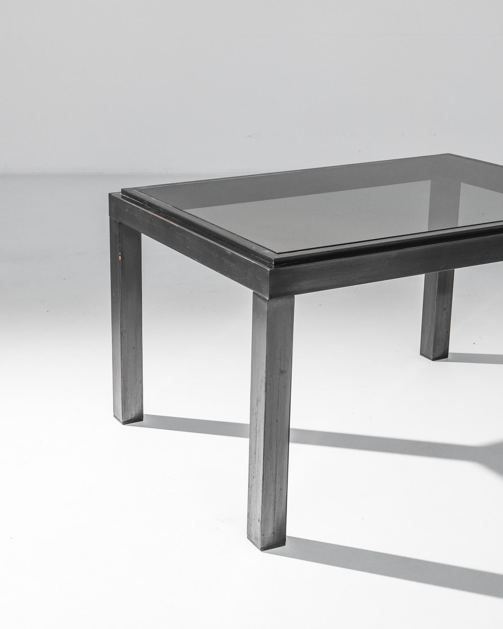 A metal table with glass top from France, produced circa 1970. Strict rectangular pillars hold aloft a darkened glass top in this distinctive table. With its ultramodern chrome silhouette, this table holds within itself dreams of constant progress