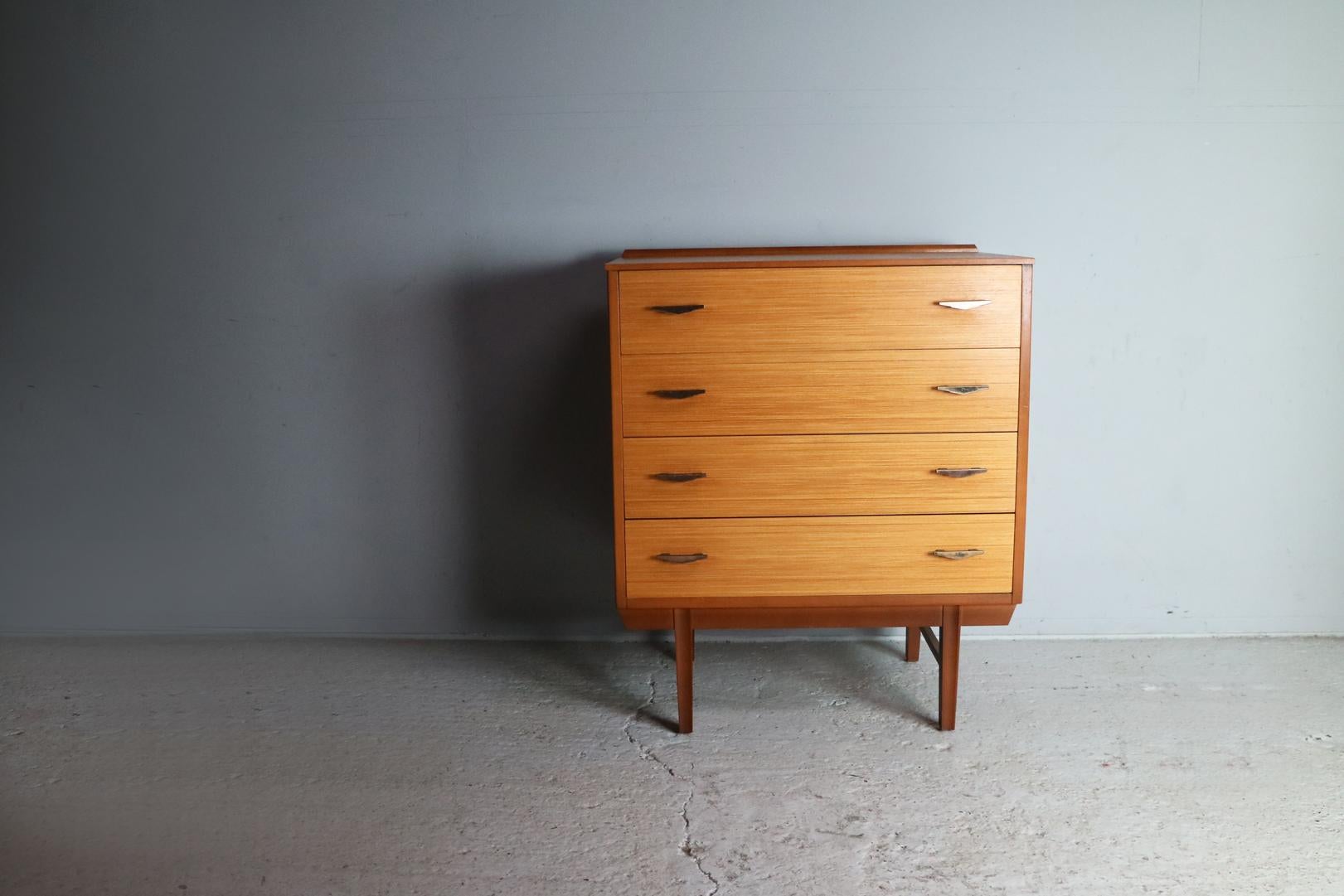 A chest of drawers very French in style. With light teak veneered drawers with a contrasting surround in darker teak. Nicely shaped brass plate handles. A very elegant piece.