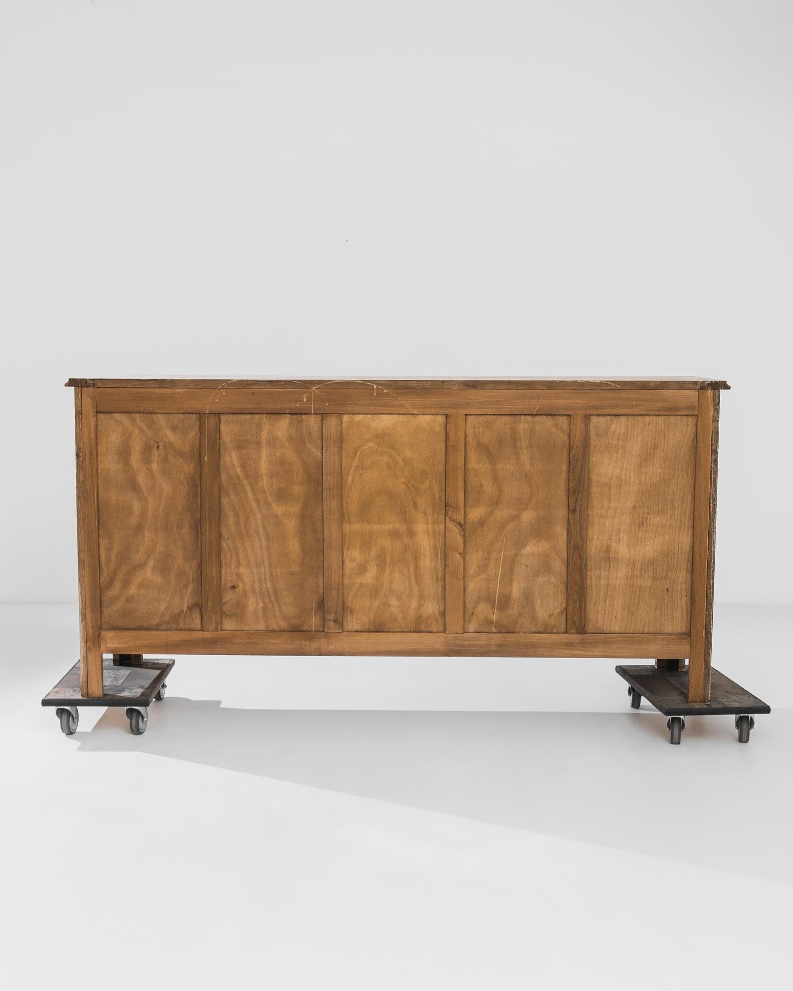 This corpulent oak buffet, crafted in France circa 1970, features four exquisitely carved doors and two complimentary drawers. The hypnotizing relief carvings on the doors bring about a three-dimensional feel. The ornate iron hardware complements