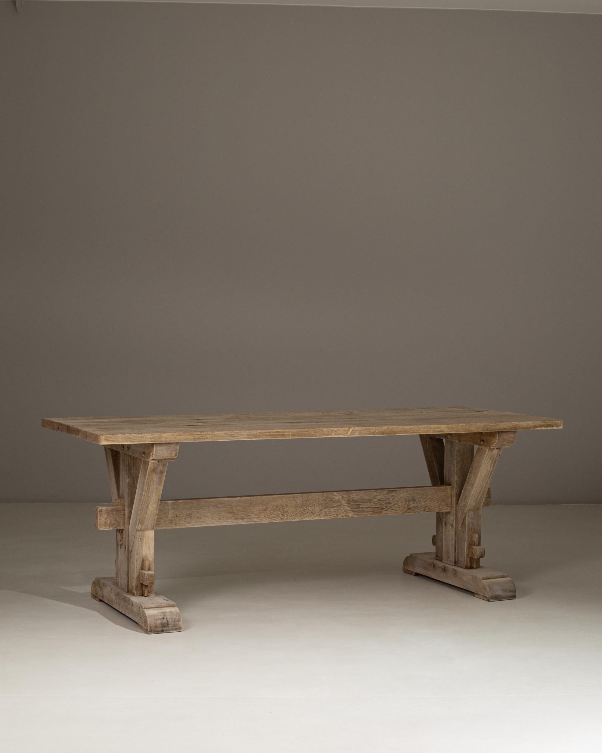 This 1970s French oak trestle dining table showcases a beautifully weathered surface and a striking architectural base that reflects the rustic craftsmanship of provincial design. The thick rectangular top rests on sturdy V-shaped supports, joined