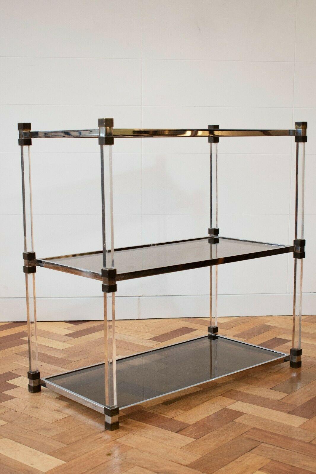 A sleek and stylish 1970's French perspex, brass and tinted glass three tier shelving unit by Etagere.

Comprising of three different materials, this shelving unit is a perfect example of sleek simplicity and would work in any interior. 

The smoked