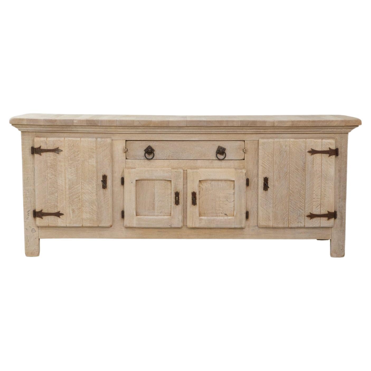 1970s French Primitive Oak Buffet With Iron Hardware. This substantial buffet showcases the rustic strength and handcrafted appeal of French primitive design. Built from solid oak, it features thick panelled doors and a central drawer, all accented