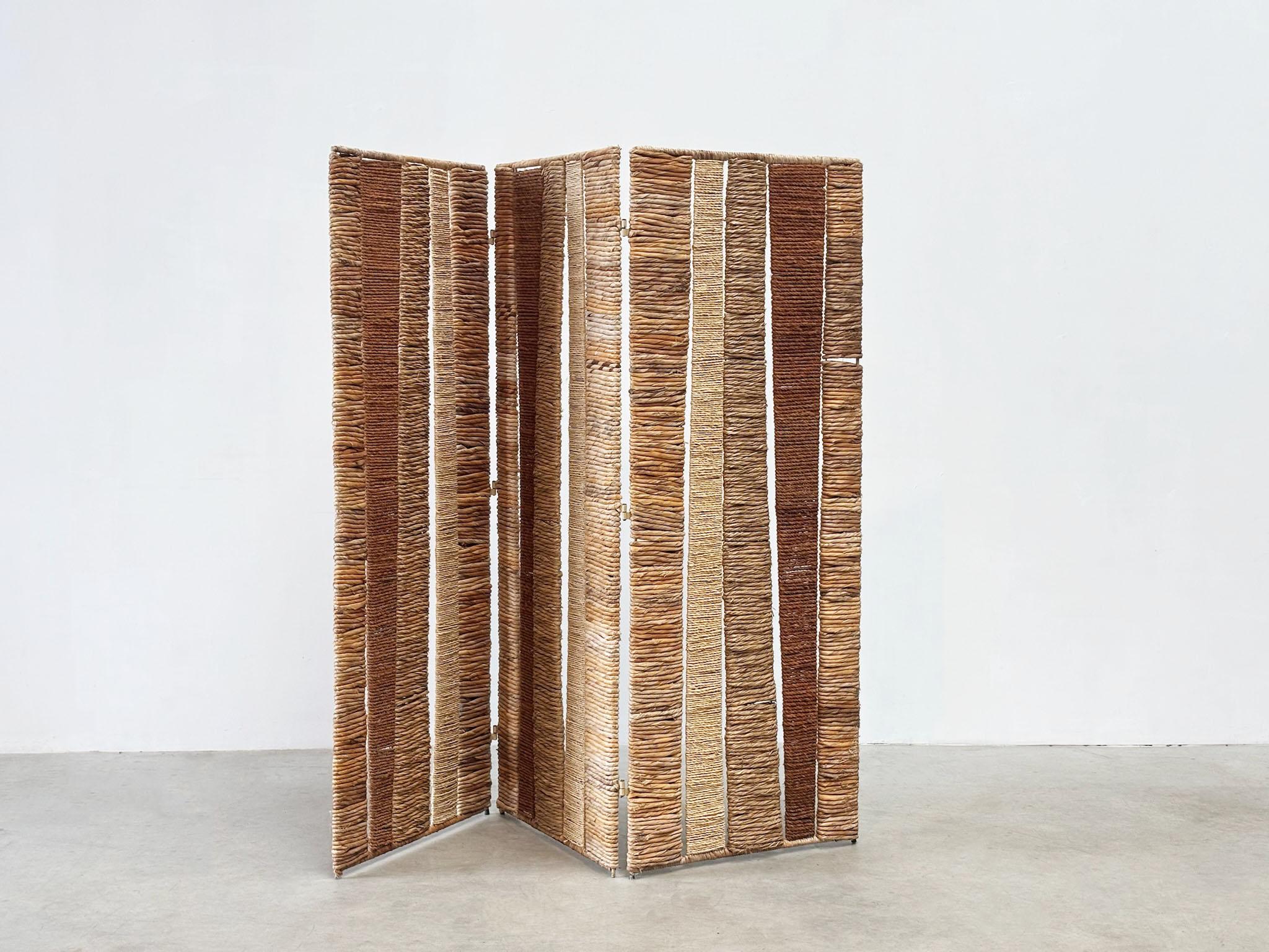 Questo divisorio francese degli anni '70, realizzato con una struttura in ferro e pannelli in rattan e corda intrecciata, richiama fortemente lo stile distintivo di Audoux Minet.
Anche se il designer rimane sconosciuto, il pezzo incarna l'estetica