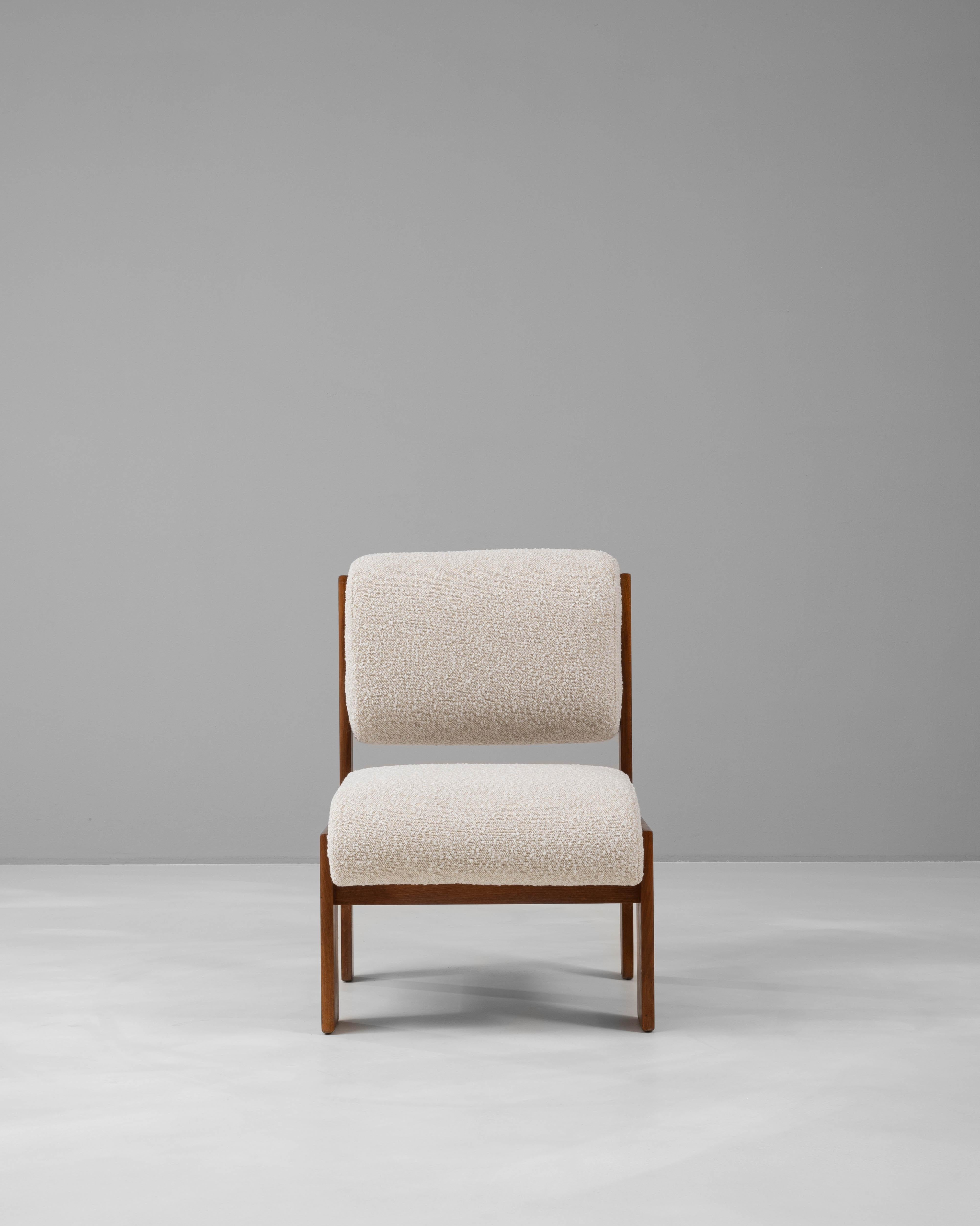 This 1970s French upholstered chair captures the minimalist elegance of mid-century design with its clean lines and timeless appeal. The chair is framed in rich, warm wood, providing a sturdy base that contrasts beautifully with the soft, textured