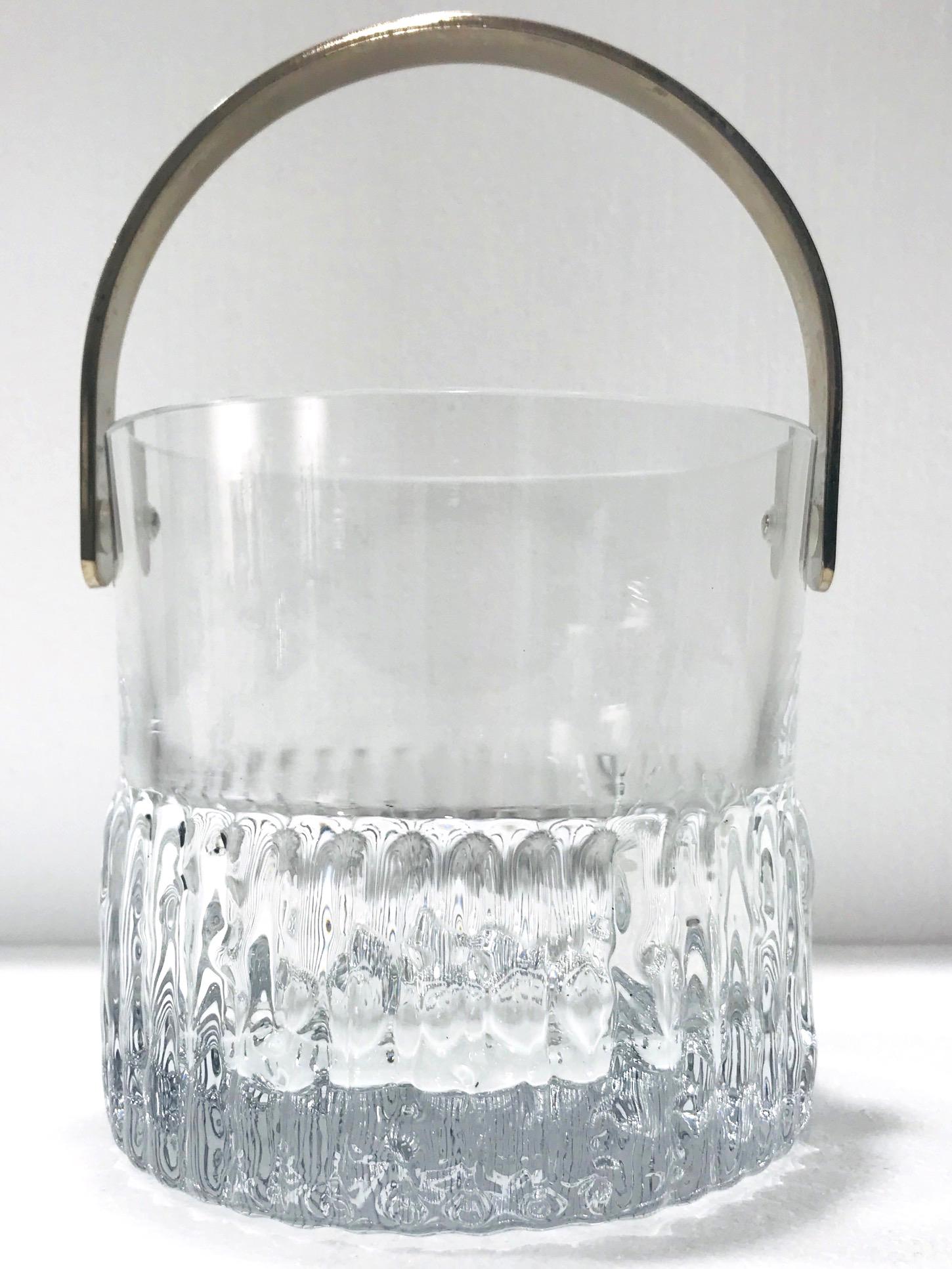 Mid-Century Modern crystal ice bucket with polished edges and stainless steel handle. Features heavyweight handcrafted crystal with fluted edges along resembling icicles or ice cubes, and with ripples on the bottom base. Makes a chic addition to any
