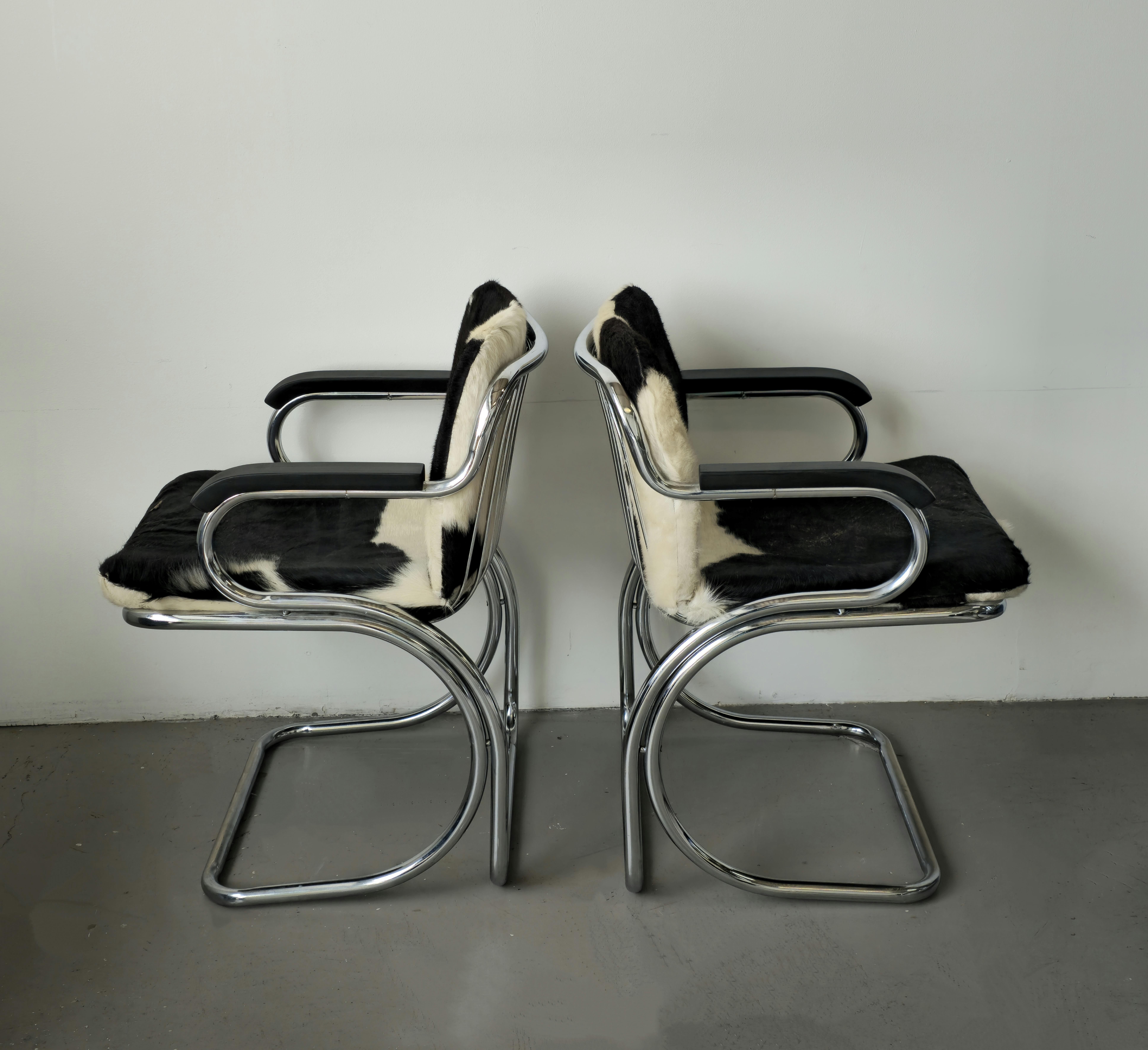 Stunning sculptural Gastone Rinaldi chrome chairs made Italy in the 1970s. These cantilevered arm chairs feature a chrome body and Cowhide cushions. The arms were refinished with black stain to match the Cowhide cushions. 
In fair condition, the