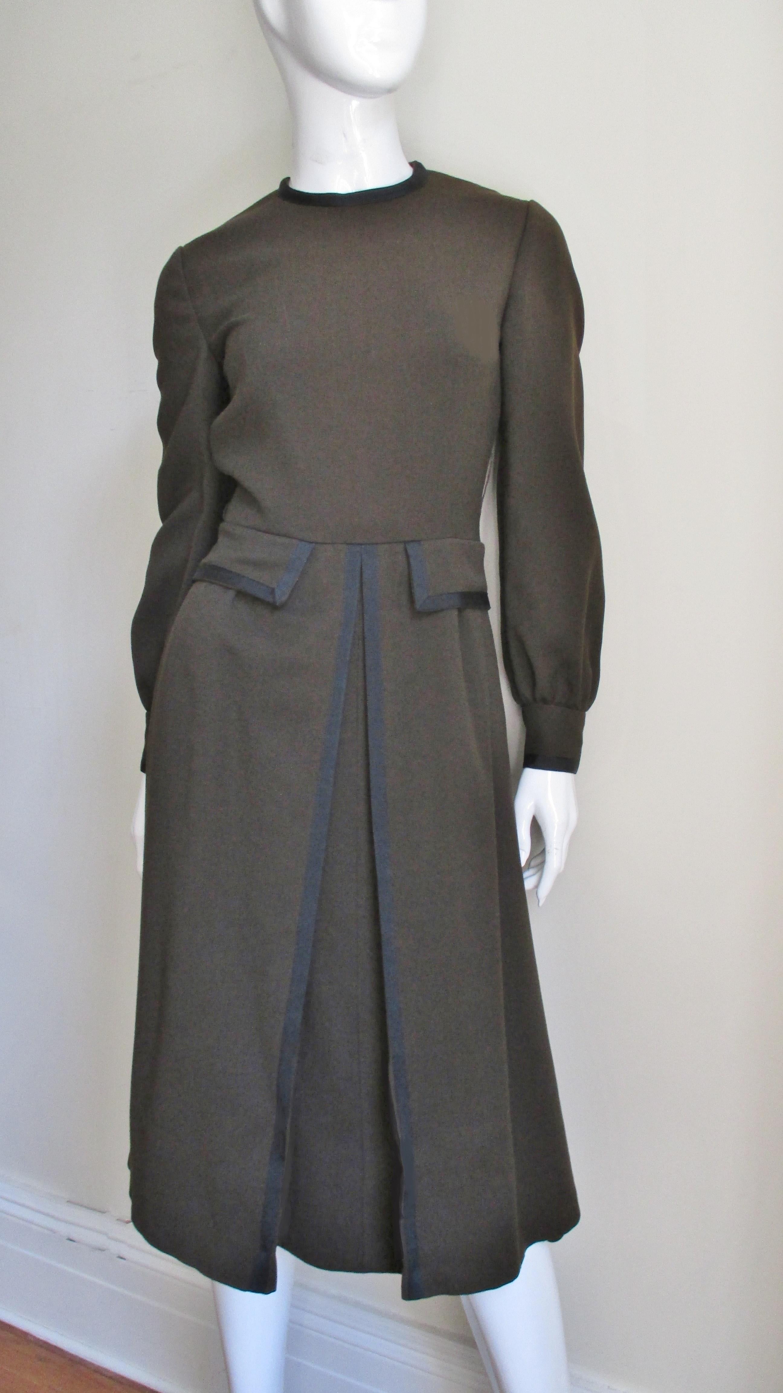 A beautiful brown wool dress with black trim from Geoffrey Beene. It has a crew neckline and long sleeves with black button cuffs. The bodice has pocket flaps at the waist and functional pockets in the skirt side seams.  The A line skirt has an