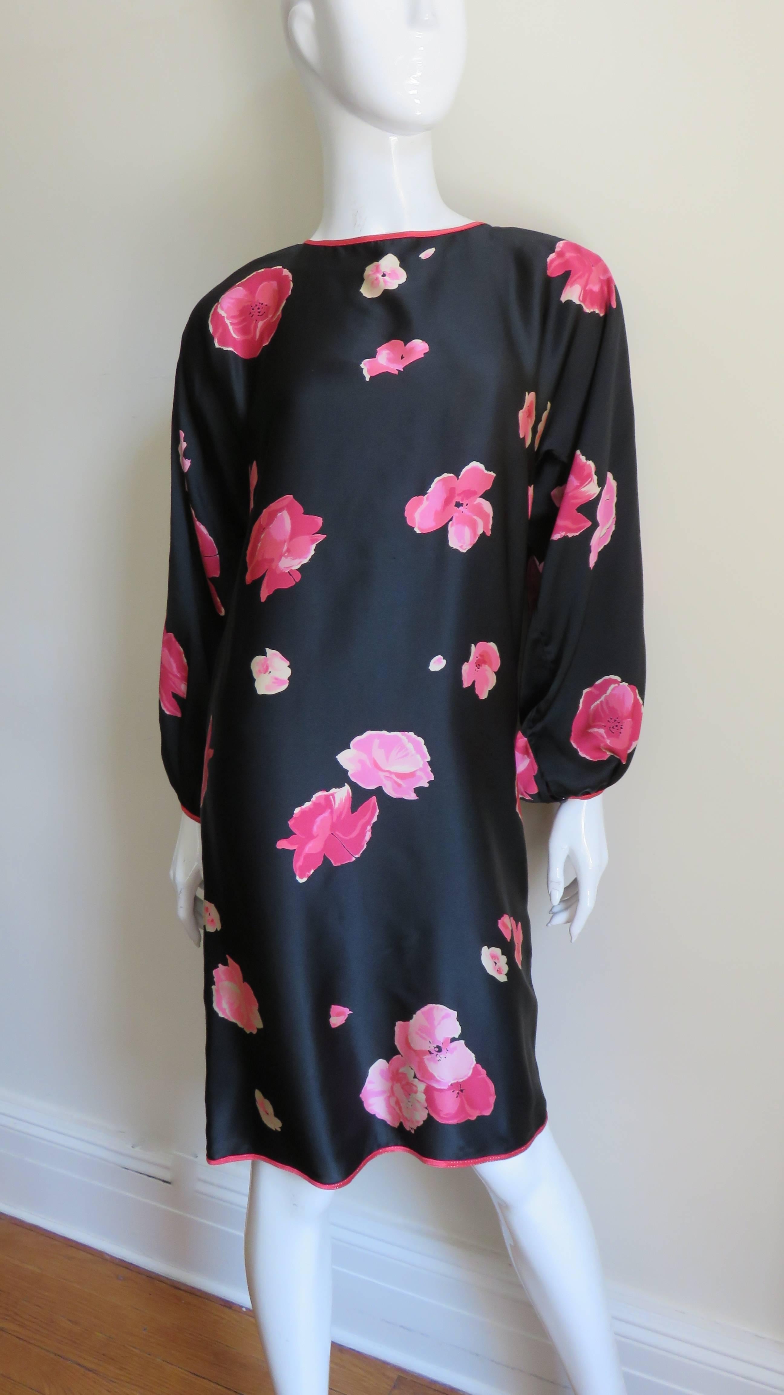 A simple black silk sheath dress from Geoffrey Beene with a pink flower print. It has a crew neckline, dolman balloon sleeves with a button closure at the wrists and falls straight to the hem.  There is an opening at the back with a tie at the neck