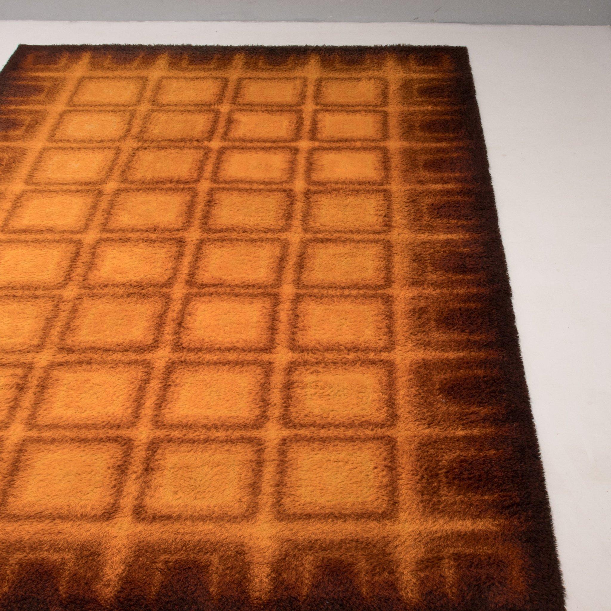 Fantastique exemple du design des années 1970, ce tapis à poils ras présente un motif graphique dans des tons de jaune, d'orange et de marron.

Le tapis est fabriqué à partir d'une laine à poils ras imprimée de carrés géométriques au centre, qui