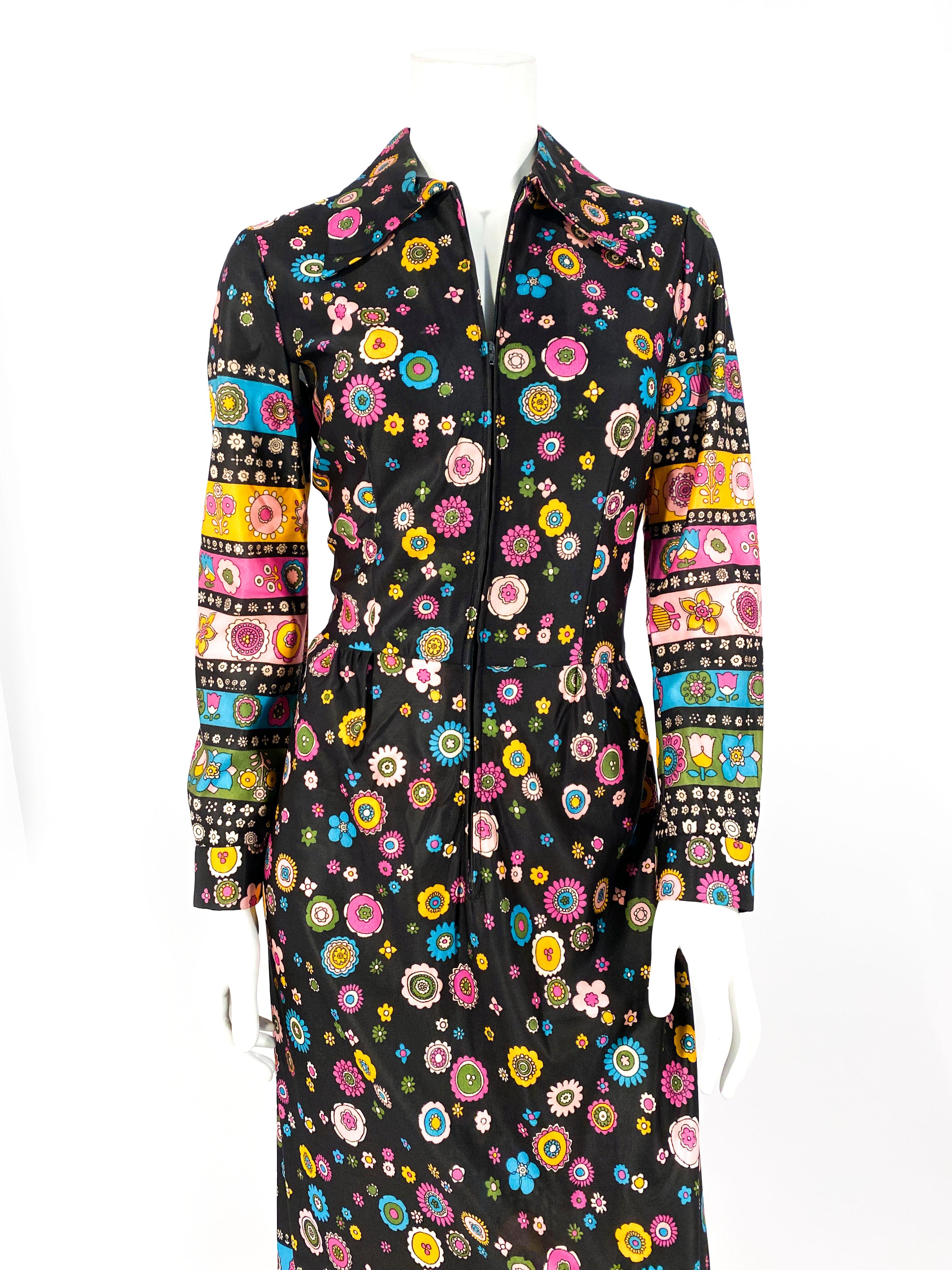 1970s printed polyester dress featuring a geometric floral print in tones of light blue, yellow, pinks and whites on a black background color. The print has several layers of boarder print along the full cuffed sleeves and at the hem on the bottom
