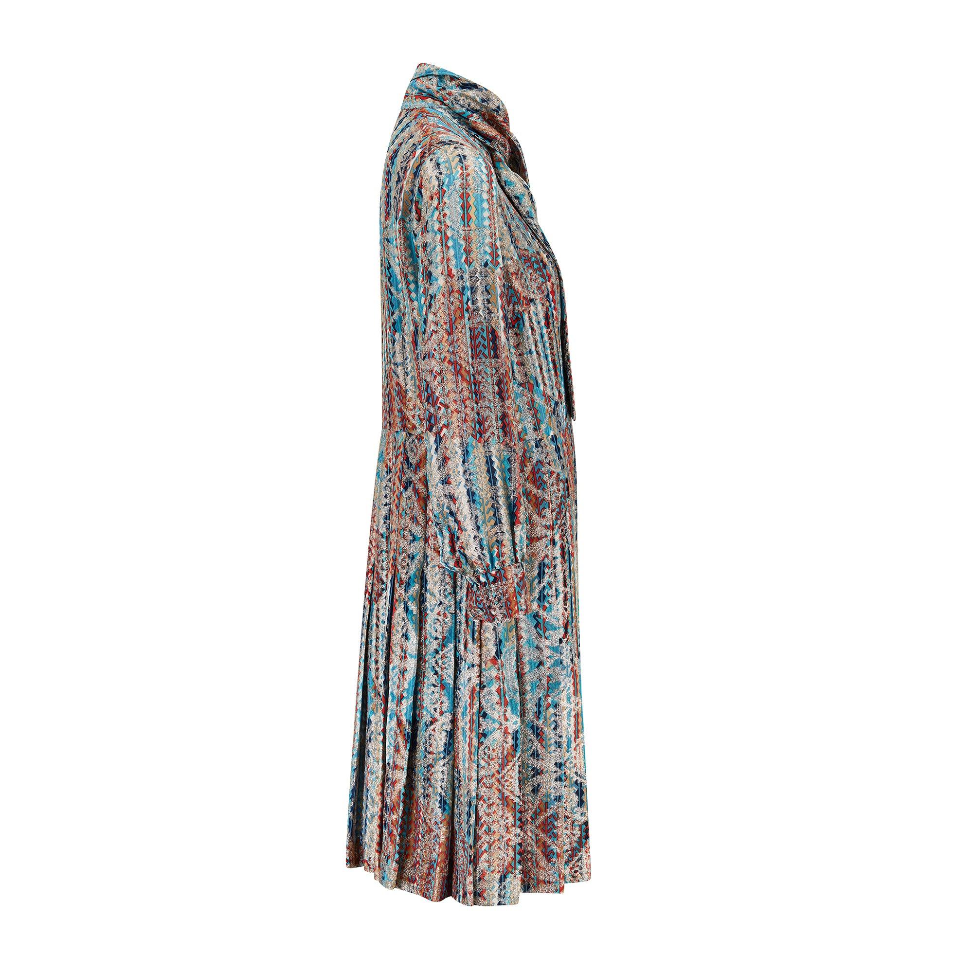 This 1970s dress is tailored to a casual, shirt-dress style that contrasts the flamboyant, metallic-streaked cloth. It has a button-down front that fastens with coordinating fabric-covered buttons. The neck has a wide tie that can be knotted at the