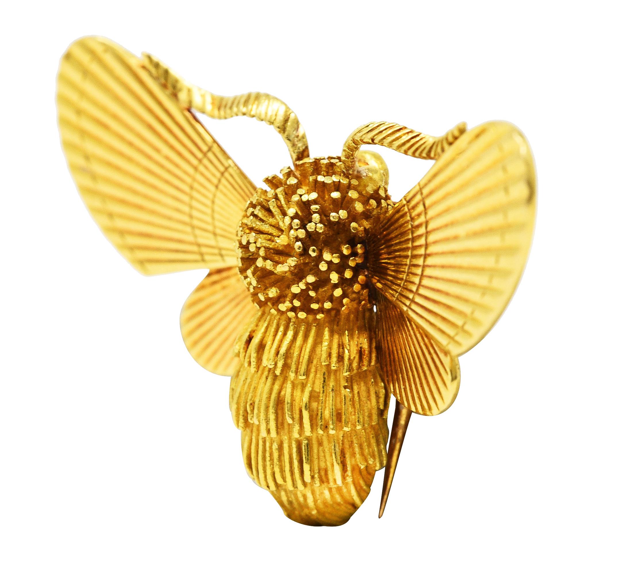 Designed as a highly stylized bumble bee with ridged fur layers on body and stippled head. Featuring fanning wings with engraved linear pattern throughout. Accented by wavy antennae with engraved texture. Completed by hinged double pin stem with
