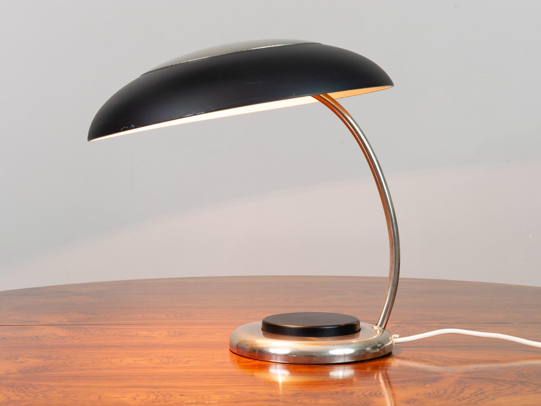 1970s German black and chrome desk lamp. A large single black on and off button sits within the chrome base. A single screw in E27 bulb sits underneath the circular canopy. The chrome curved stem connects the shade to the base. The desk lamp is in