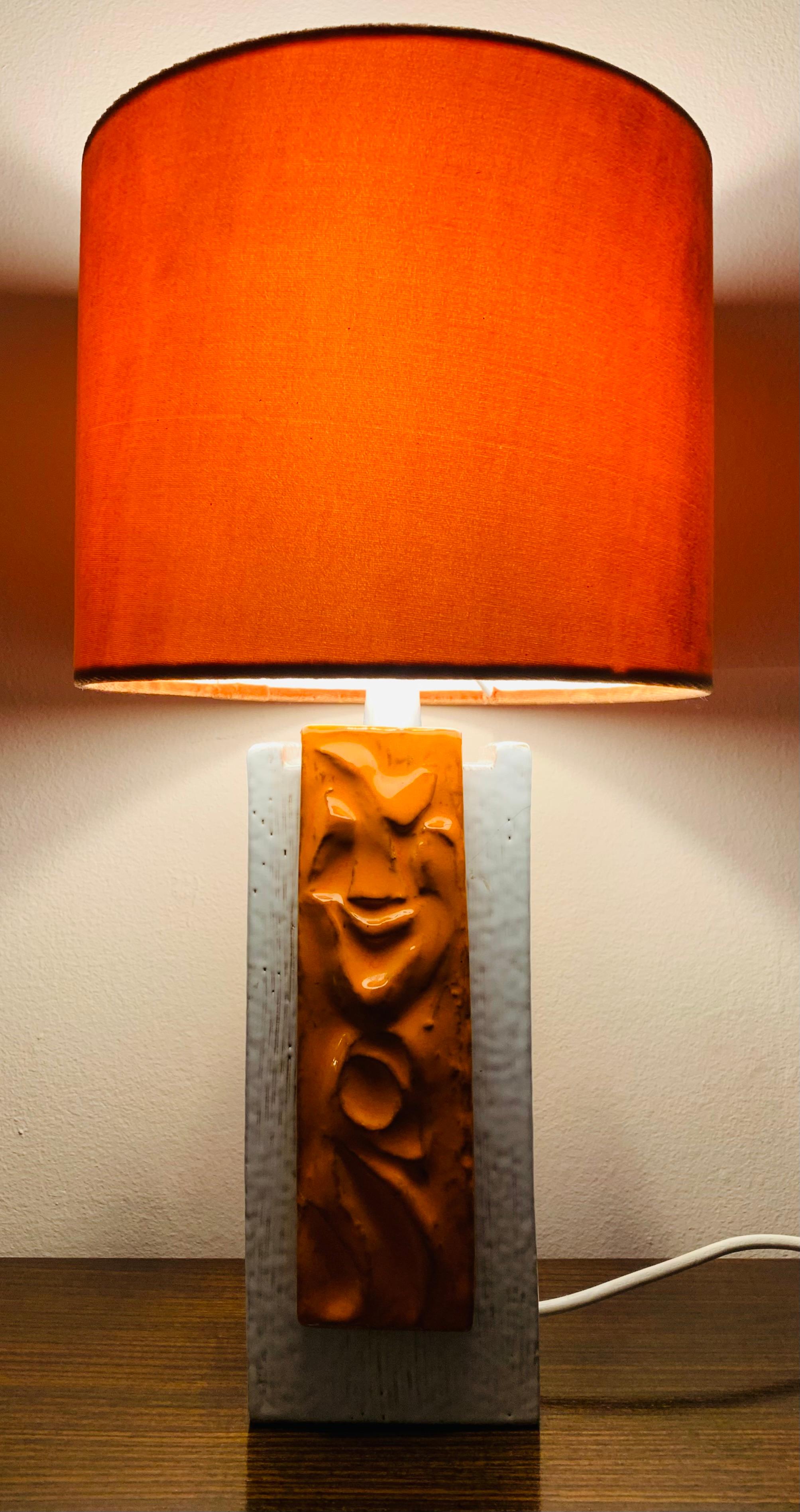 1970s German ceramic table lamp including a velvet orange shade. An orange glazed feature abstract 3-D tile sits on opposite sides of the square white base with vertical incised lines. In very good vintage condition. The lamp has been rewired with a