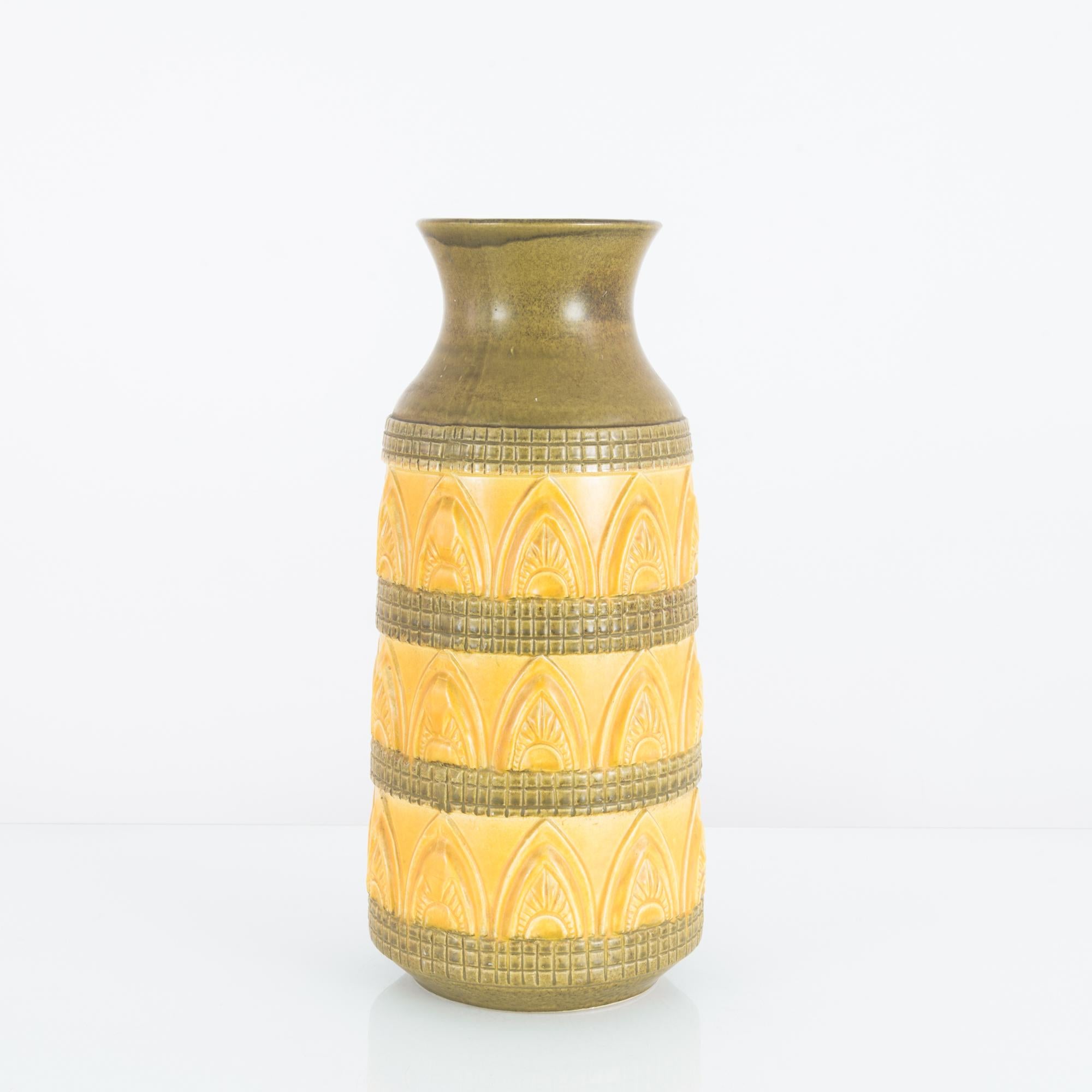A ceramic vase from Germany, produced circa 1970. A ceramic vase in beautiful earth tone bands of muted cornflower yellow and Xanadu green. Decorated in Art Deco inspired bas relief of sunburst motifs inside pointed double arches resting on a raised