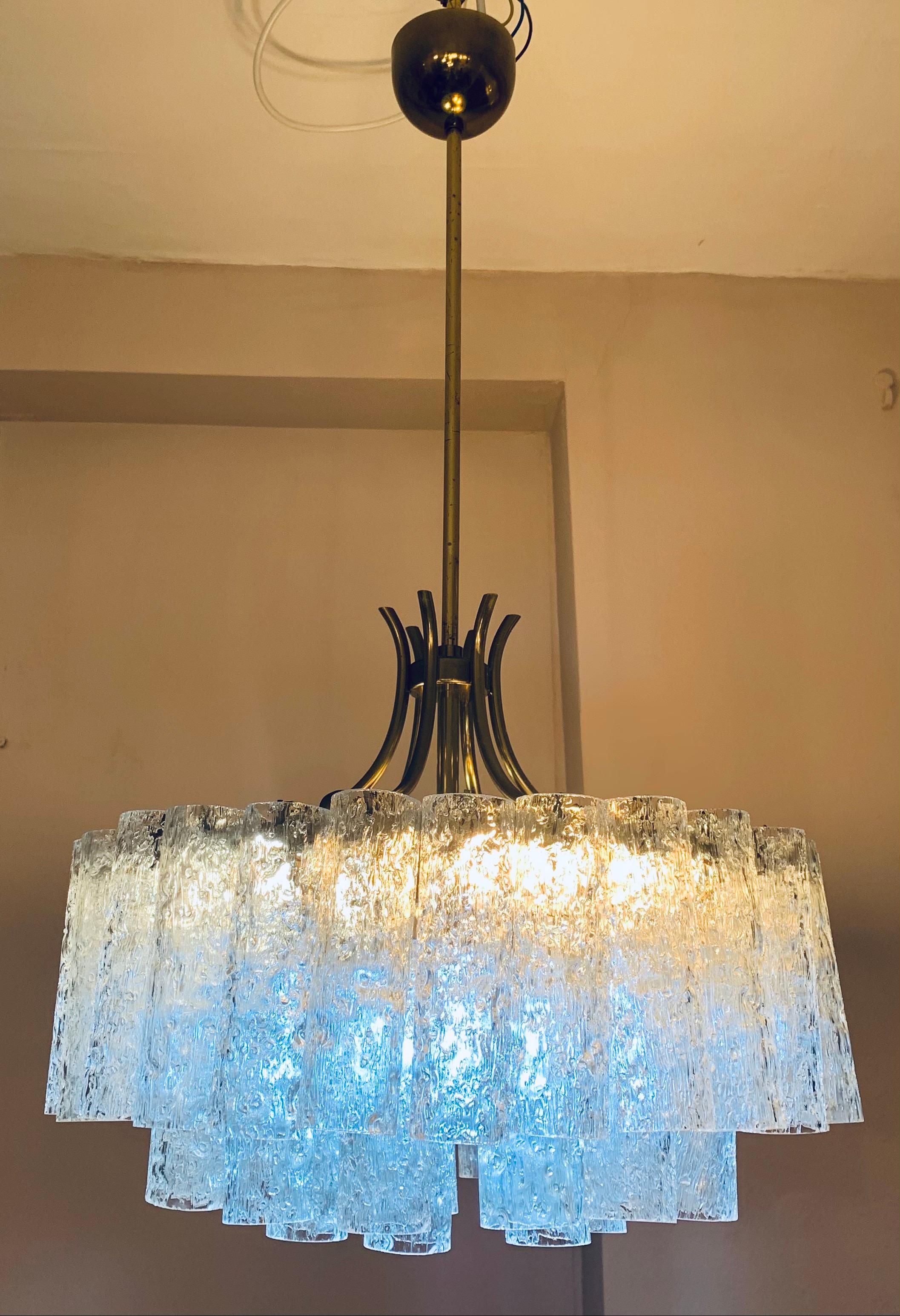1970s mid century textured clear glass tubular glass chandelier. Manufactured in Germany by Doria Leuchten. The three-tier glass tubes hang at varying heights from a tubular brass frame. The glass tubes are all the same diameter. The stem can be