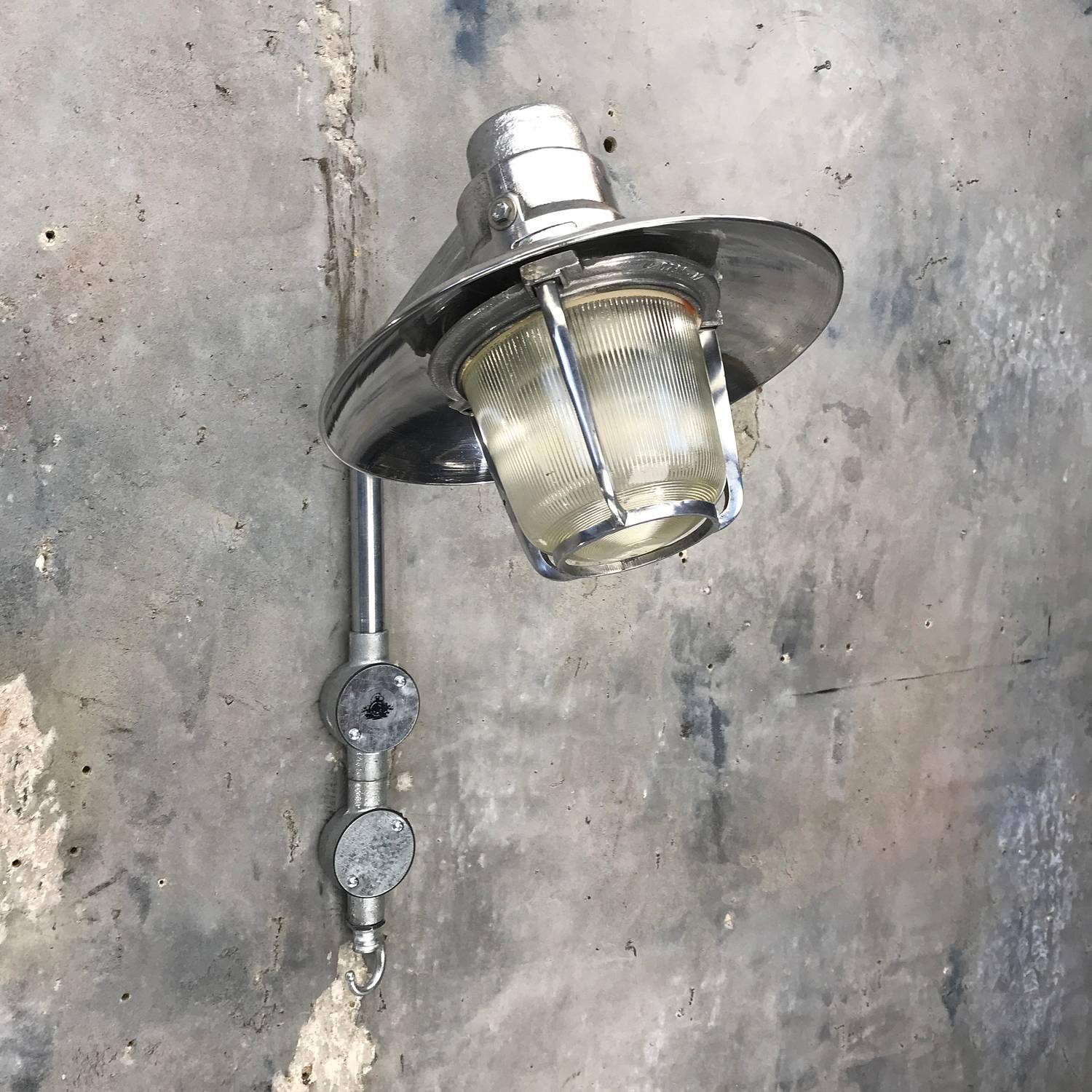 Retro aluminum wall light with prismatic glass shade.  Reclaimed from cargo ships and professionally restored in the UK ready for modern interiors.  

The glass is clamped down by the cast frame.  The frame and the glass turn and detach to reveal