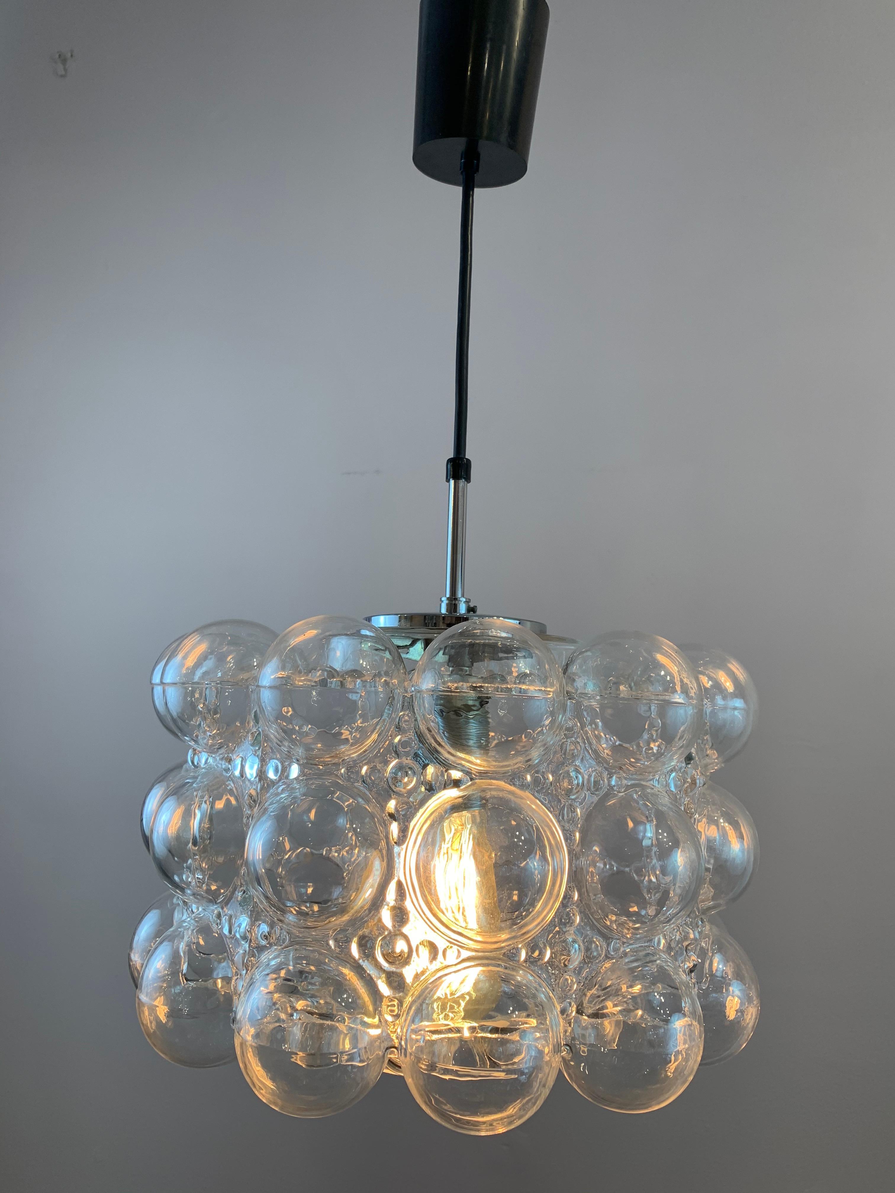 An unusual and striking German clear 'bubble' glass pendant light designed by Helena Tynell for Glashütte Limburg in the 1970s. The shade is suspended from a chrome fitting which it pushes on to allowing easy access to the bulb and for cleaning