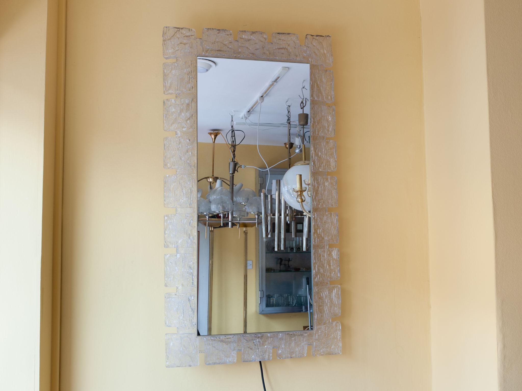 1970s German rectangular backlit wall mirror by Hillebrand. The rectangular mirror is surrounded by a frosted iced geometric frame which hook son to a white metal base which holds the bulbs behind. The frame holds 8 small screw in lightbulbs. In
