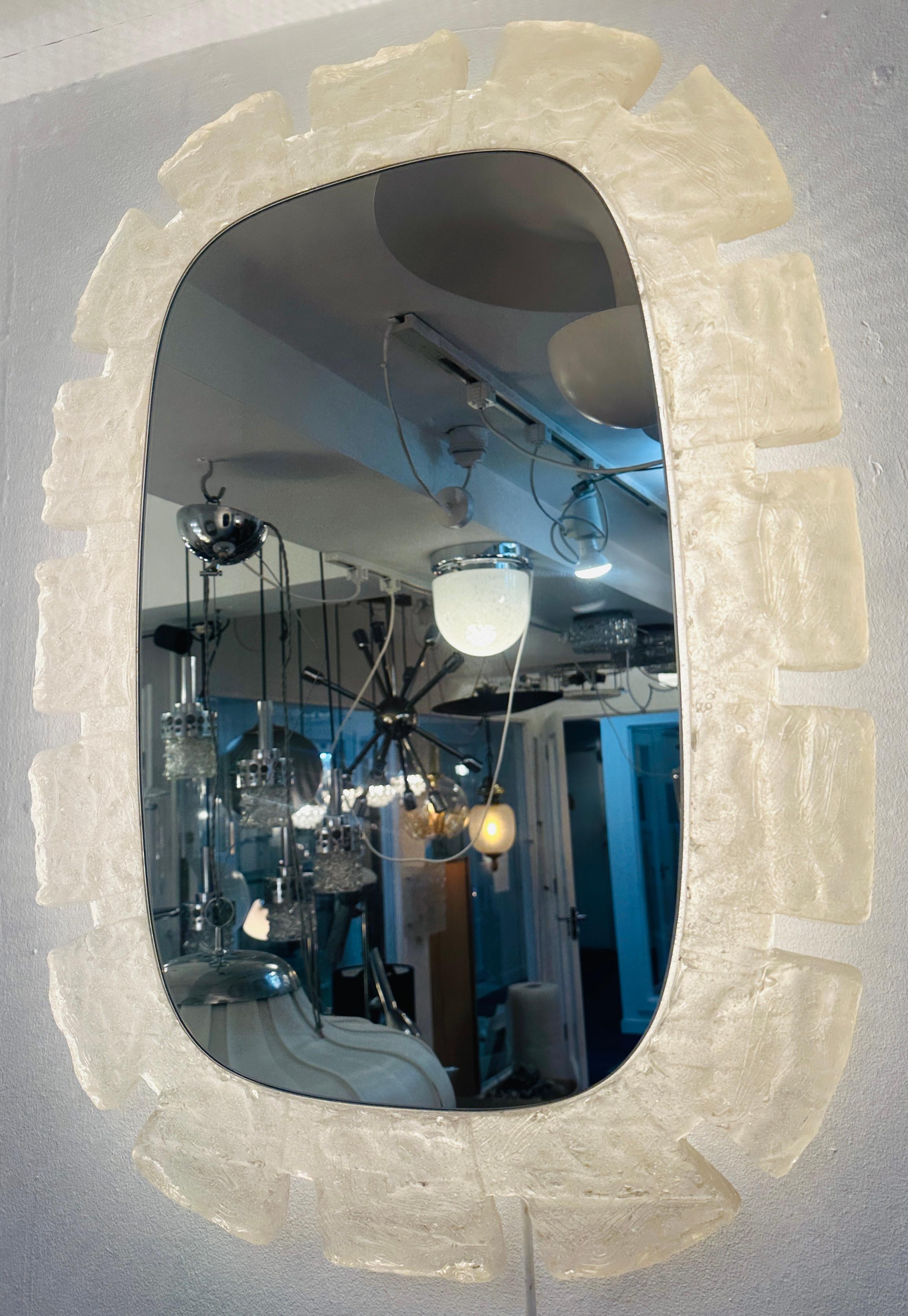 1970s German Hillebrand Leuchten oval wall mirror with a frosted translucent acrylic frame.  The acrylic frame has a stepped design reminiscent of castle turret. The mirror hooks onto a white lacquered oval metal frame which is surrounded by