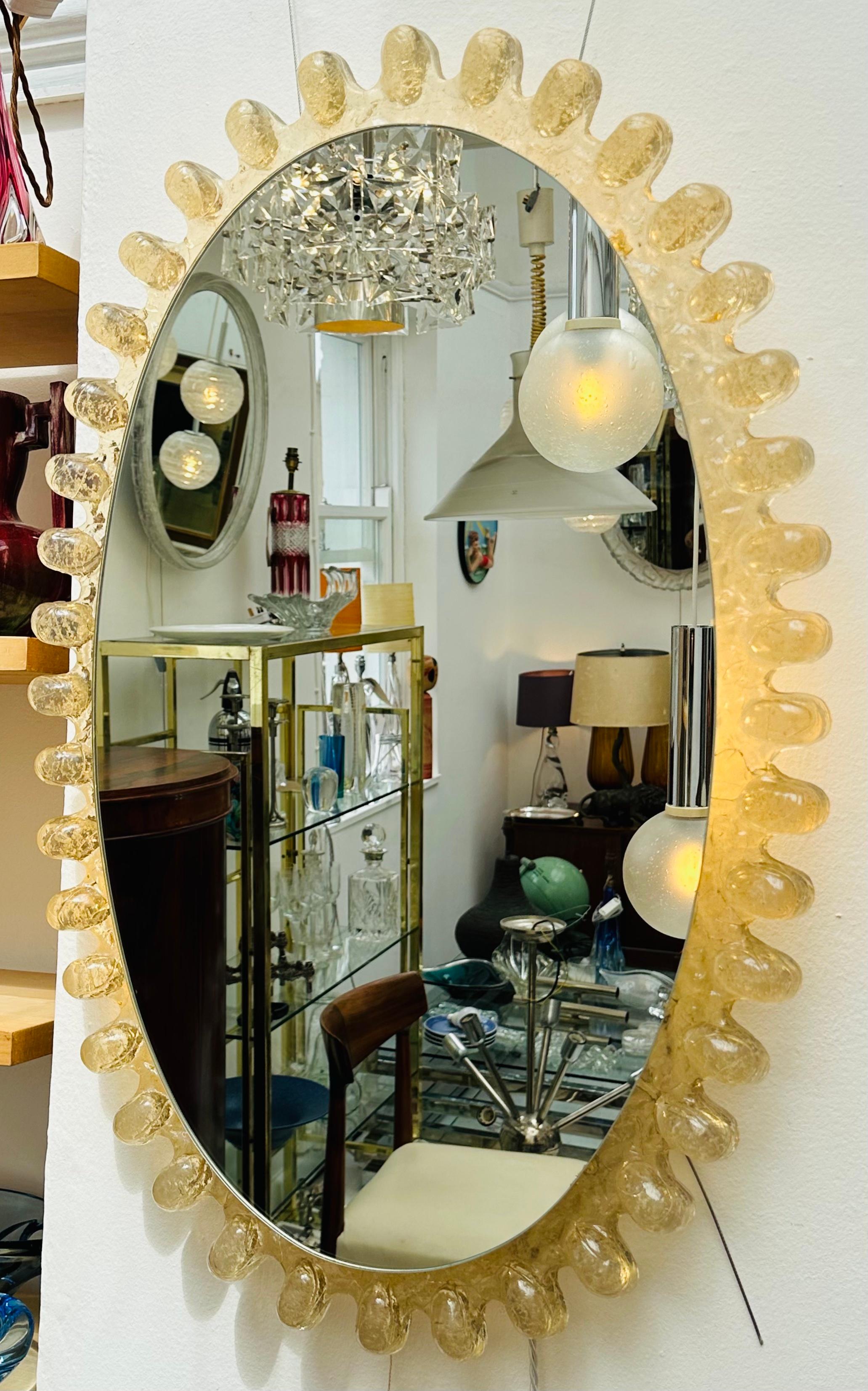 An unusual and rare to source with this design a 1970s German Hillebrand Leuchten illuminated wall mirror with a raindrop effect amber transparent lucite frame surrounding it. The mirror hangs from a white lacquered frame where the lightbulbs are