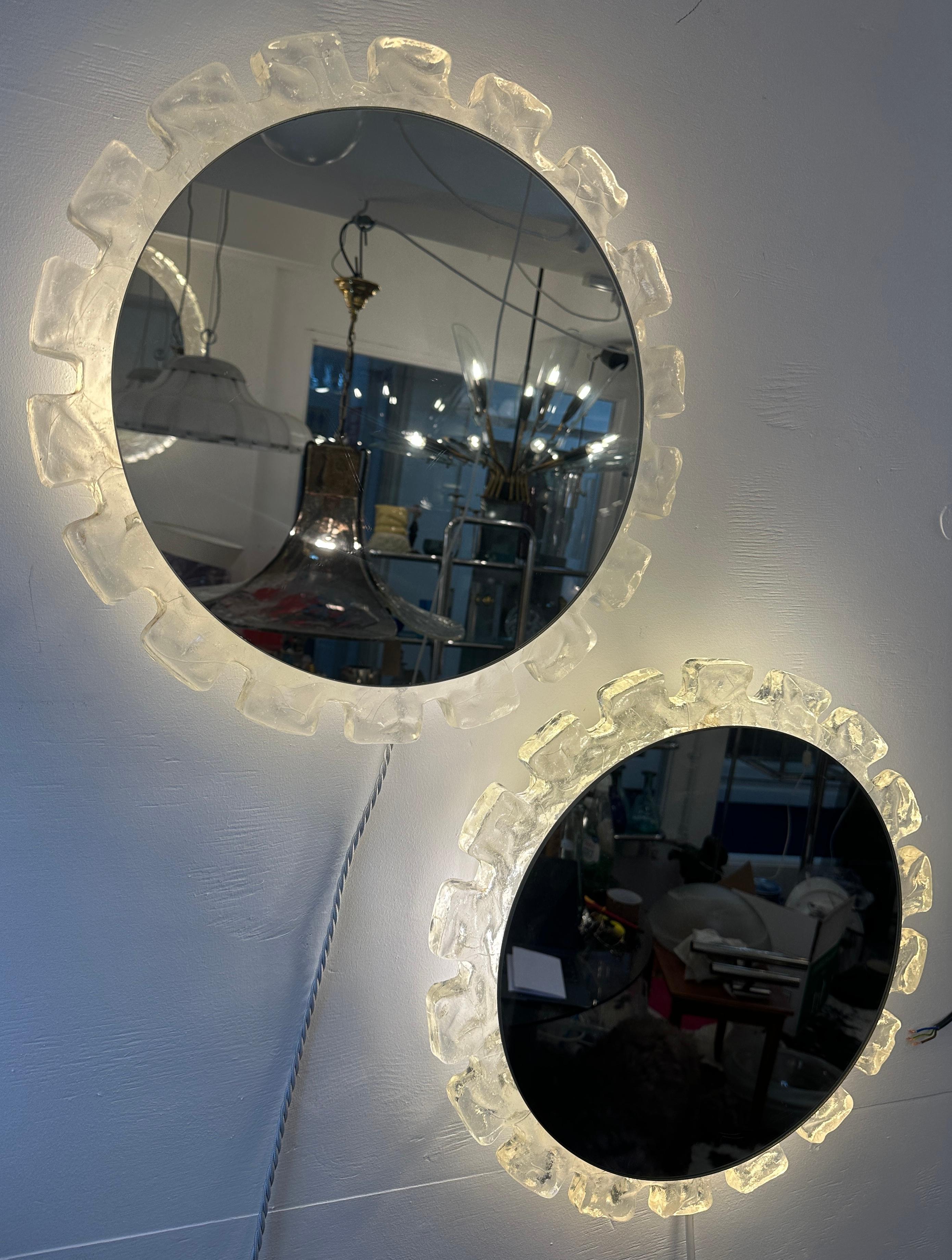Vintage 1970s German Hillebrand Leuchten circular wall mirrors featuring a unique bubbled-iced translucent stepped acrylic frame. The mirror is supported by a circular white lacquered metal frame, securely screwed onto the acrylic frame in the
