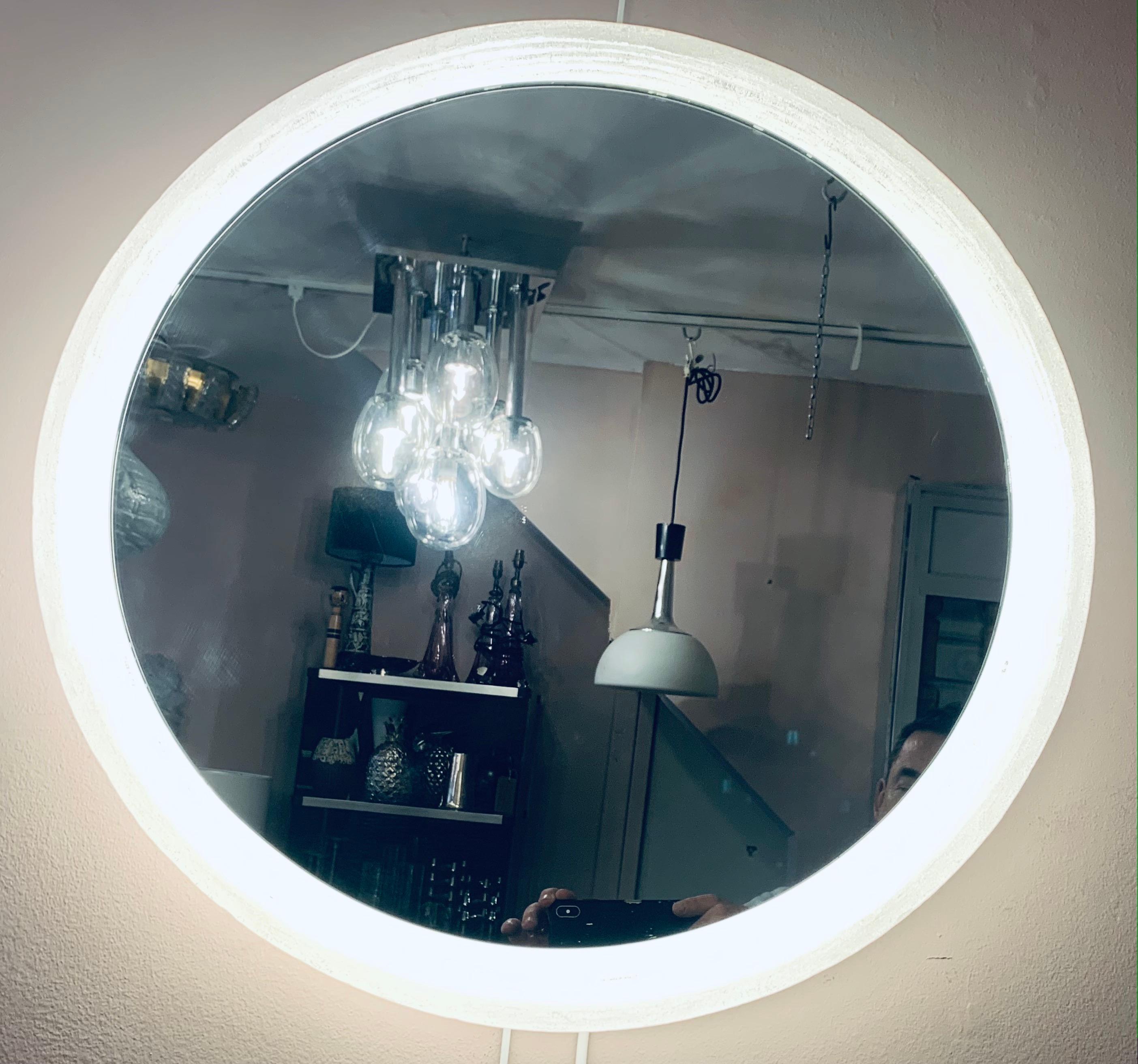 1970s German, Hillebrand lighting, illuminated, backlit, lucite-framed, circular, mirrored-glass wall mirror. The glass mirror is surrounded by a frosted-iced lucite round frame which is screwed onto it. The frame holds 5 small screw in E14 light