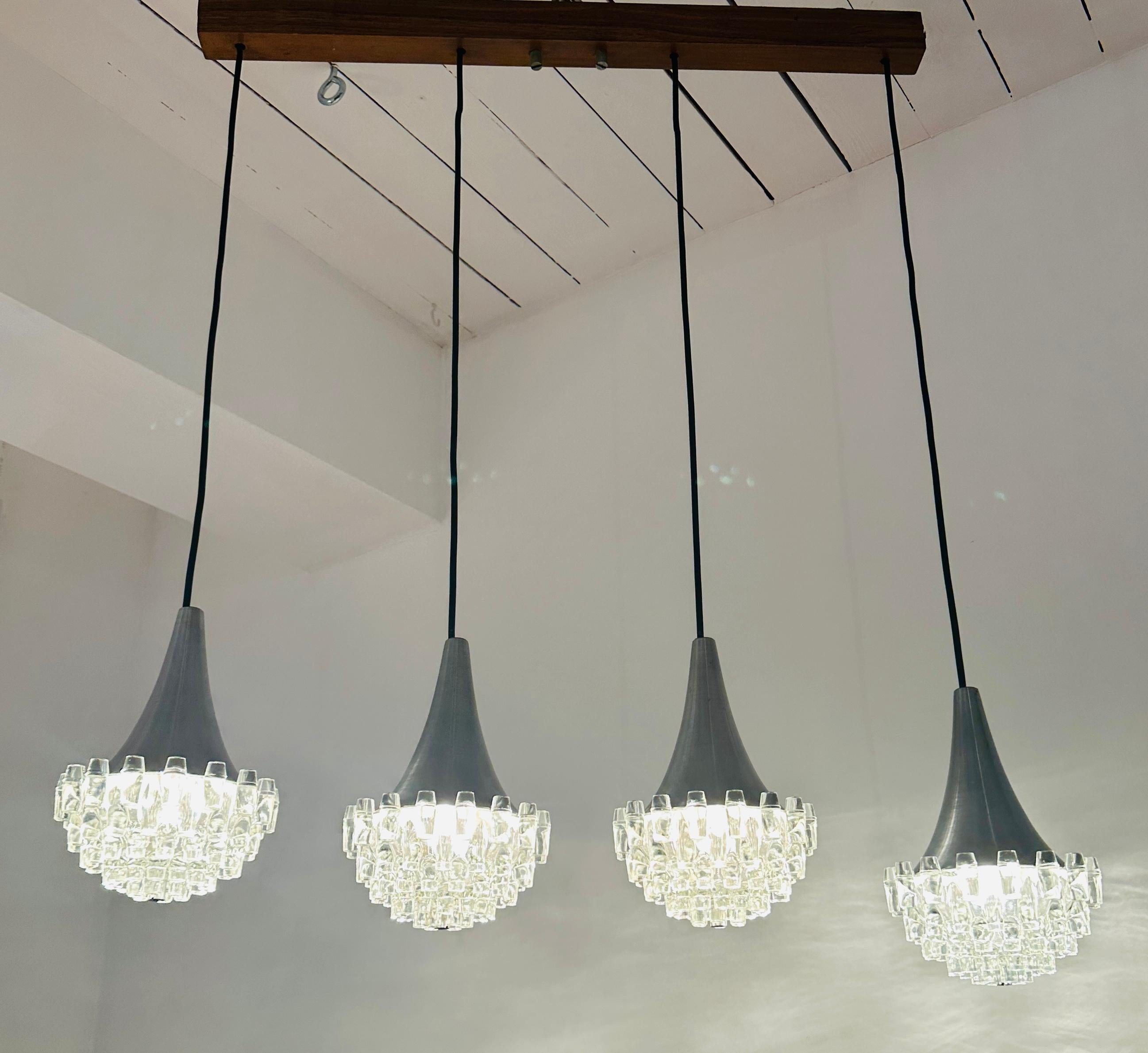 Plafonnier allemand Hudstadt-Leuchten des années 1970, composé de quatre torches en verre et de suspensions chromées.  Le Label d'origine du fabricant est toujours présent dans le plafonnier en bois auquel chaque lampe est suspendue et où les fils