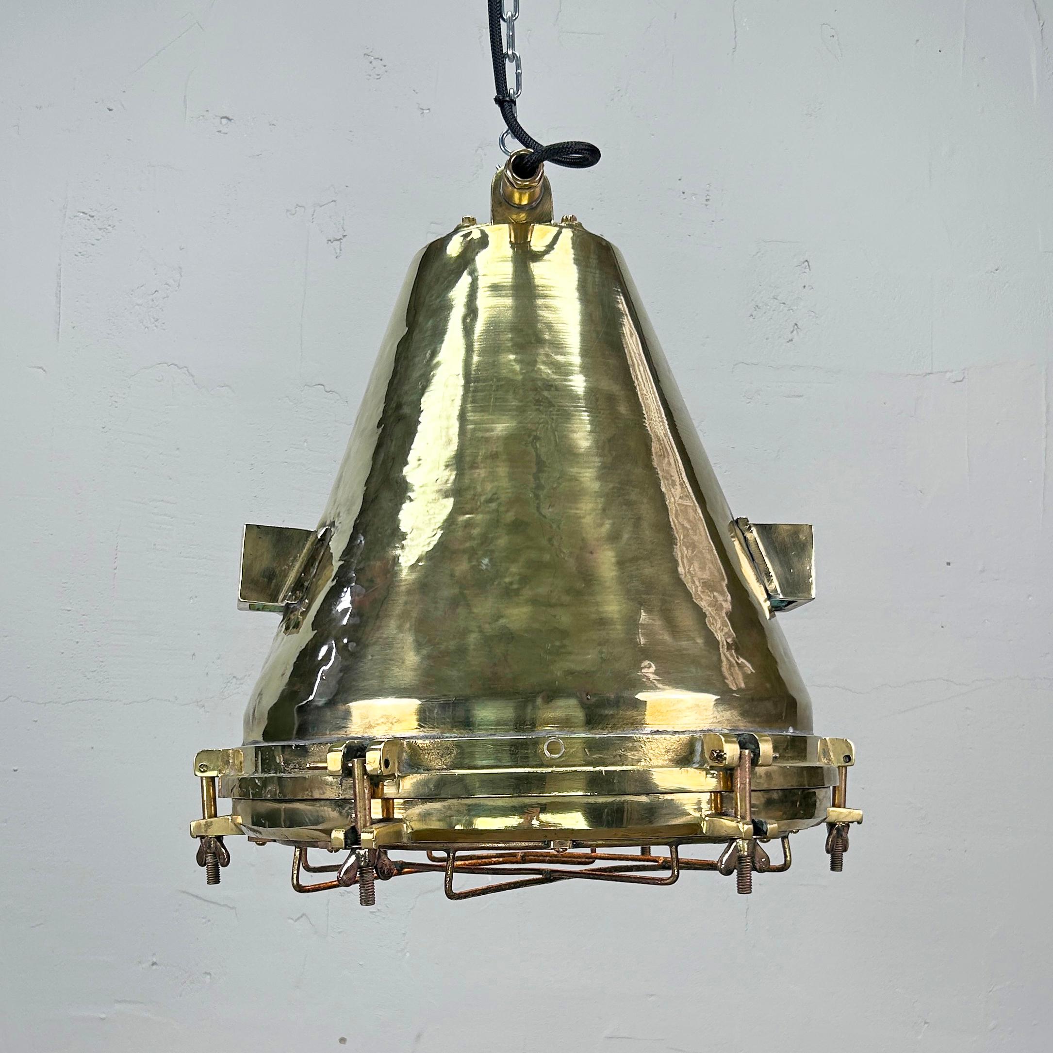 The large industrial brass ceiling light is made in Germany in the 1970's. It features a protective cage over the glass lens which protects the lamp holder. The made body of the fixture is spun brass, the fittings are cast brass with an aluminium