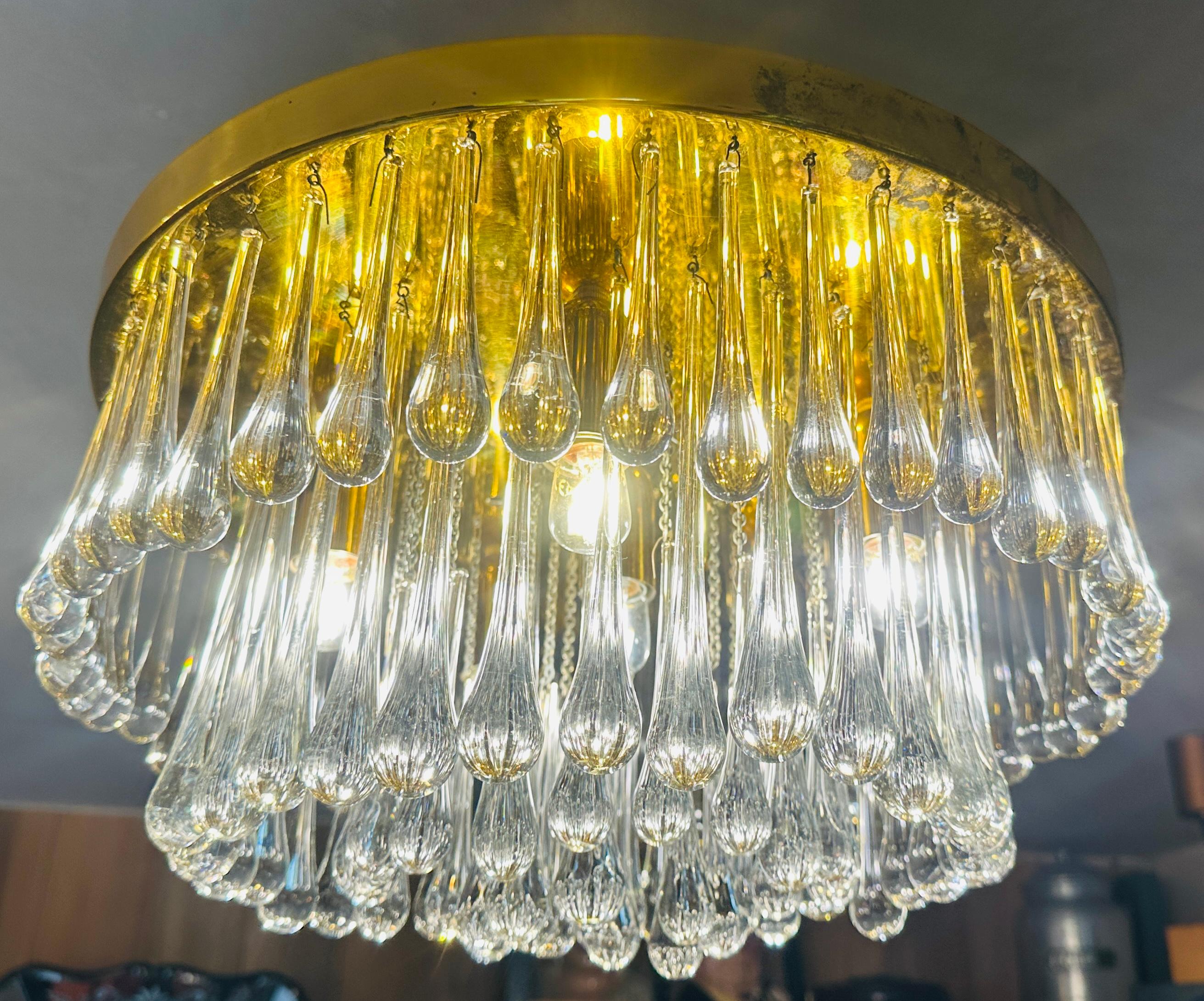 A striking flush mount ceiling light manufactured by Christoph Palme, Germany, during the 1970s. It’s composed of clear Murano teardrop glass elements on an aged polished brassed metal circular ceiling plate.  The original blue manufacturer's label
