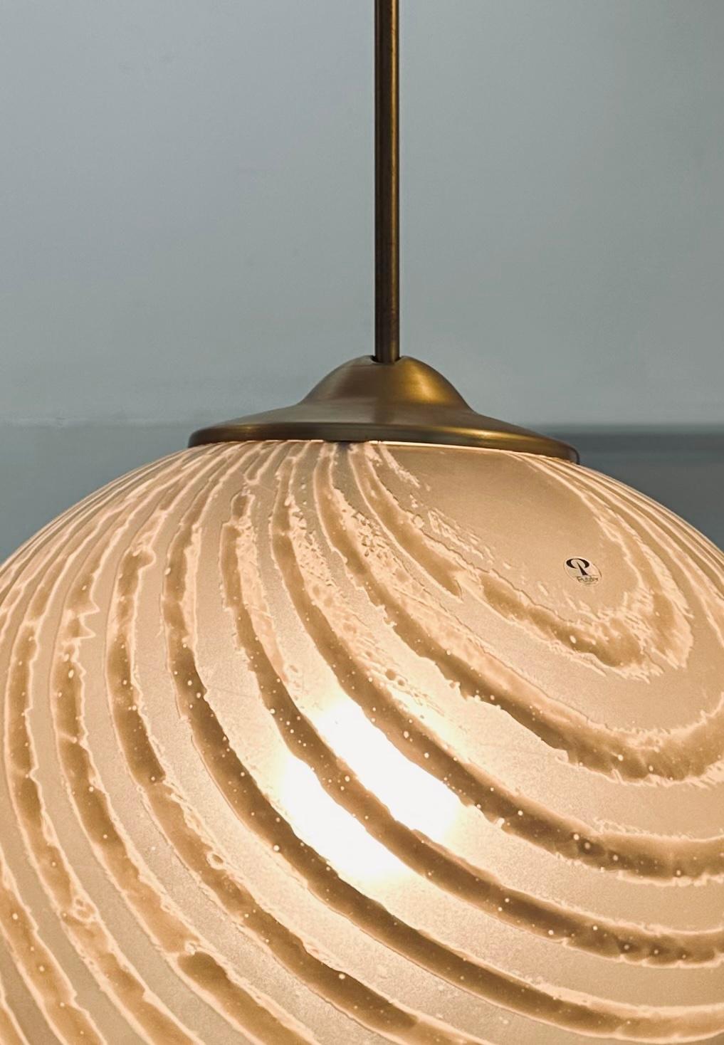 1970s German Peill & Putzler gold tinted striped satin glass hanging ceiling pendant light.  The globe appears quite different when lit with its vibrant lines of a darker shade of white running around its surface inside the globe.  The globe is