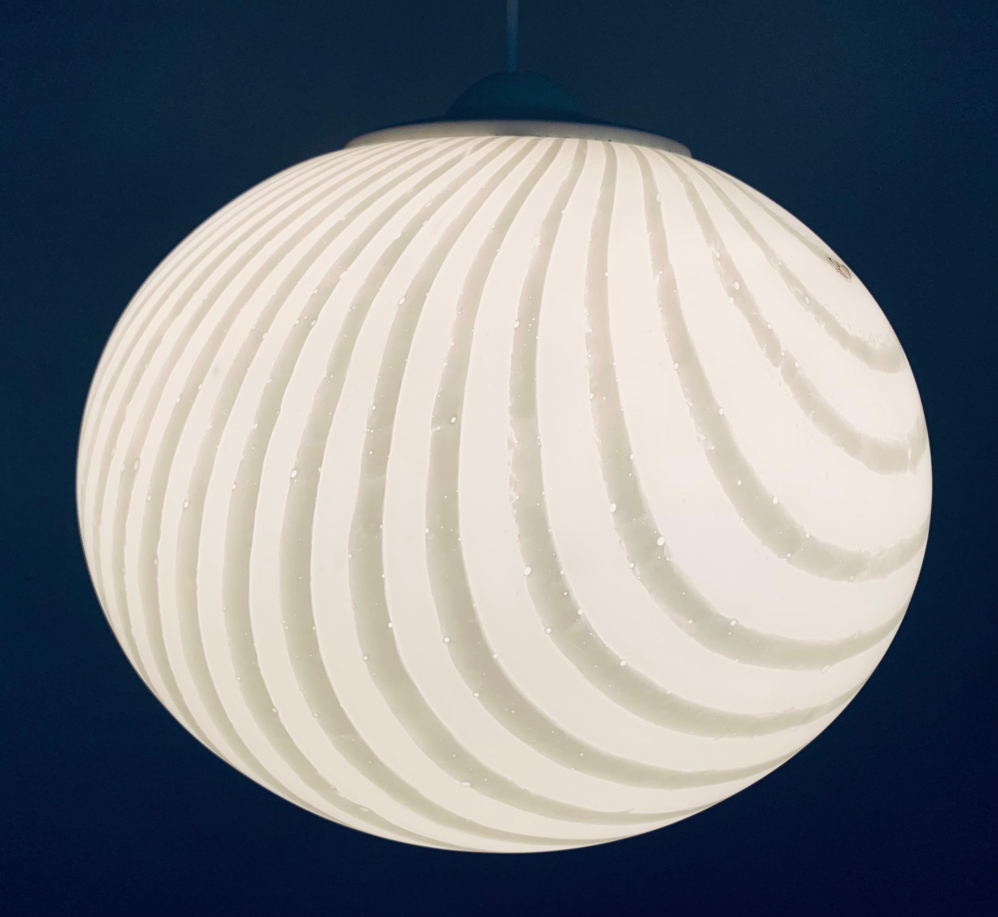 1970s German Peill & Putzler opaline hanging light. The globe specifically when lit has vibrant lines of a darker shade of white running around its surface. The globe is supported by a white bulb socket holder and held into place with three sliding