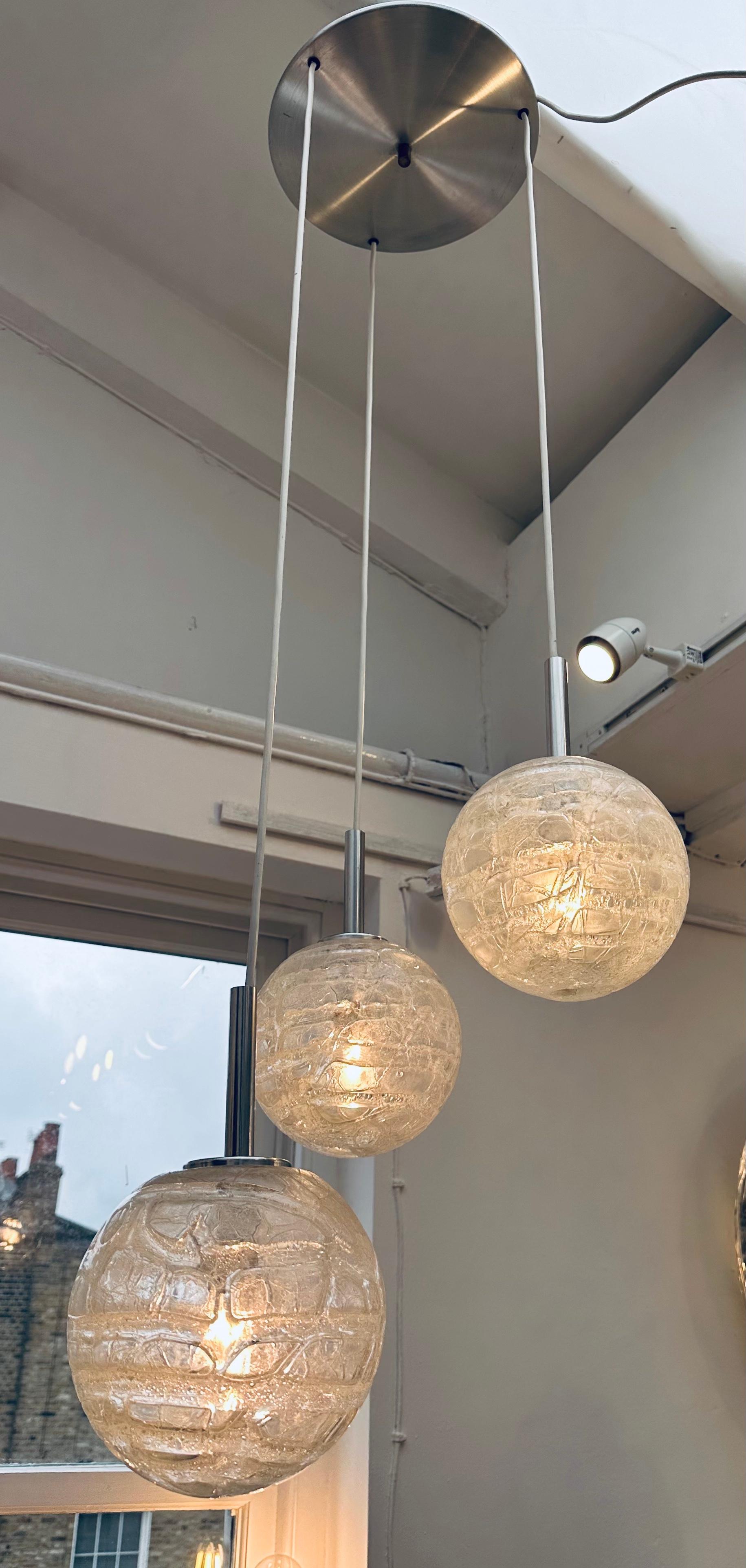 A triple globe crackled iced-glass suspended hanging light made in the 1970s by Doria Leuchten in Germany. The three equally sized cascading globe shades hang at different heights from white wires which all connect to a brushed chrome ceiling disc
