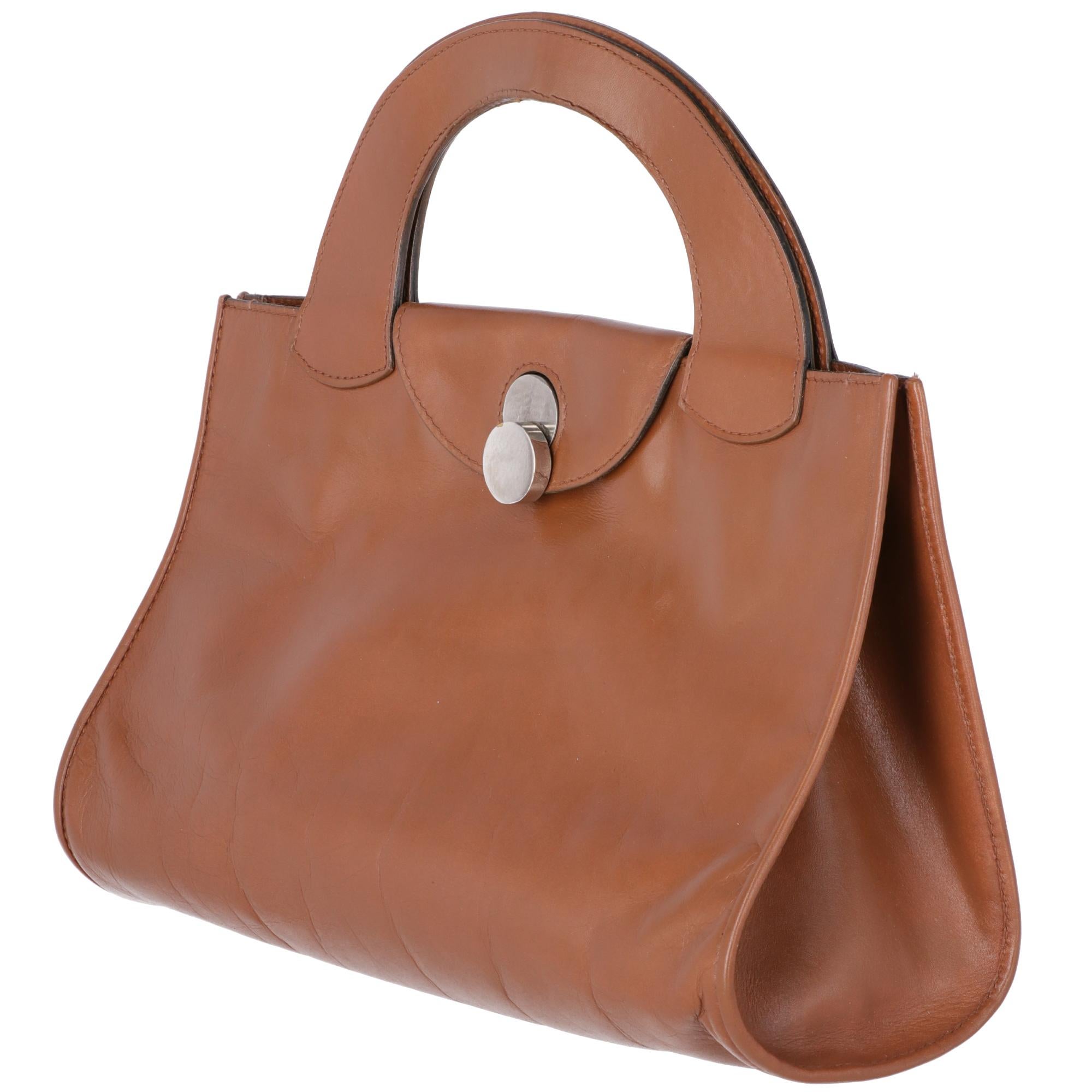 Gherardini brown leather hand bag with leather flap and metal rolling closure. Leather lining with two patch pockets, one opened and the other one with zip.

The bag has slight signs of use on the metal details, wrinkles on the leather and internal