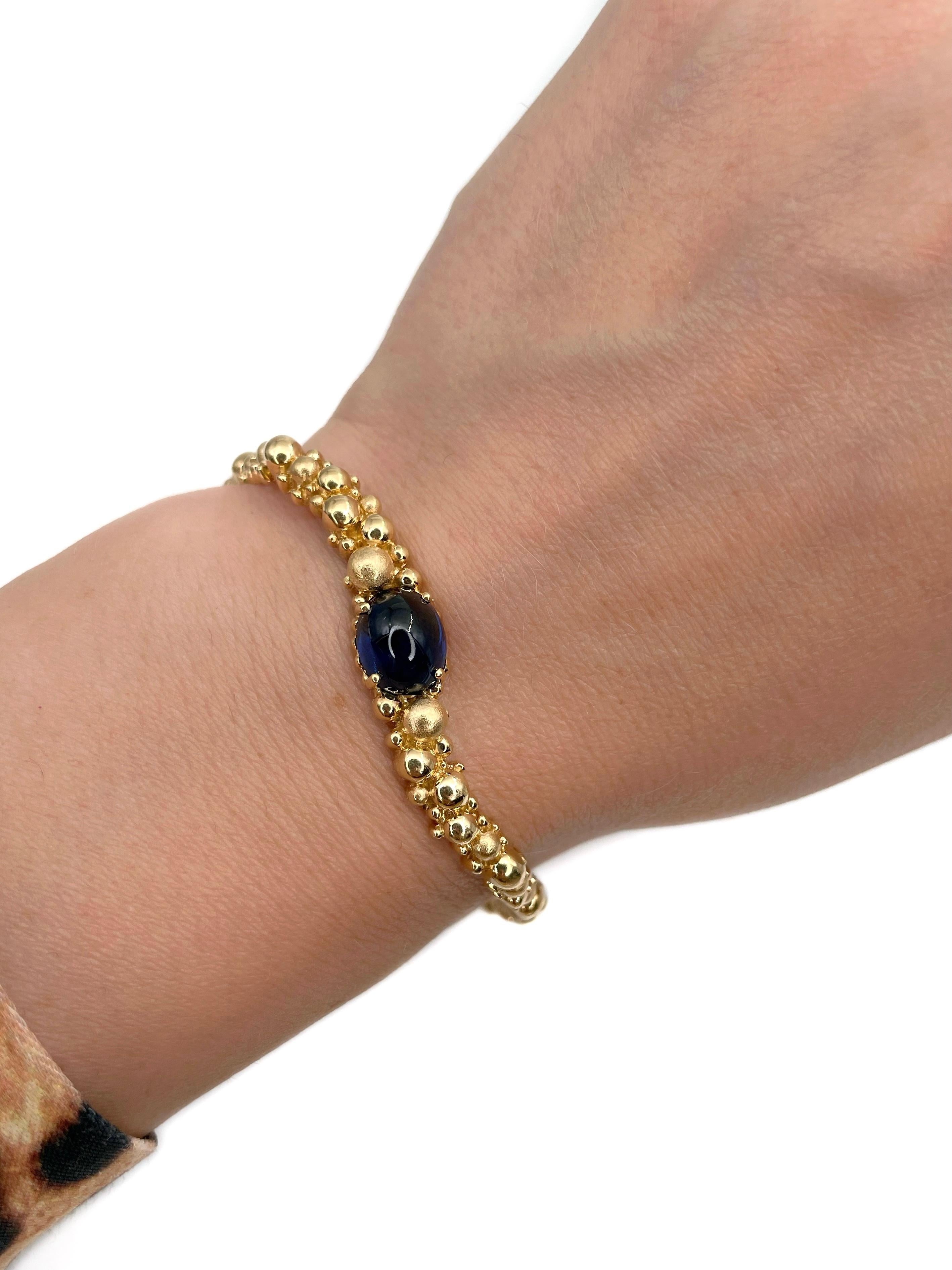 Si tratta di un bracciale bangle con cerniera con motivo a bolle. È stato progettato dal gioielliere svizzero Gilbert Albert negli anni Settanta. Il pezzo è realizzato in oro 18 carati. Il bracciale presenta uno zaffiro blu tagliato a cabochon.