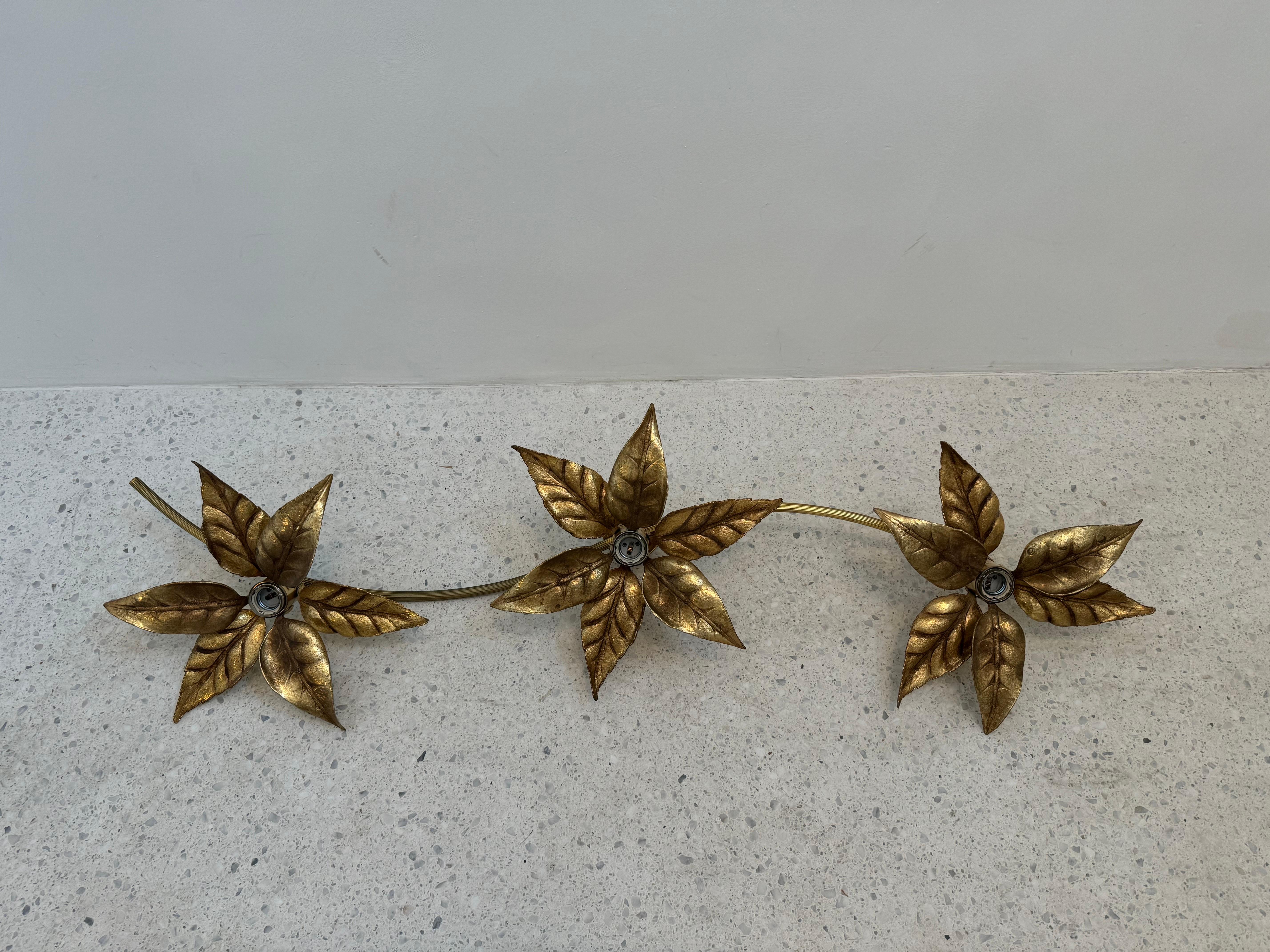 Elegante applique en métal doré des années 1970 du designer belge Willy Daros, présentant trois fleurs sculpturales avec des feuilles délicatement façonnées dans des tons dorés. Cette lampe décorative incarne le mélange signature de Daros de